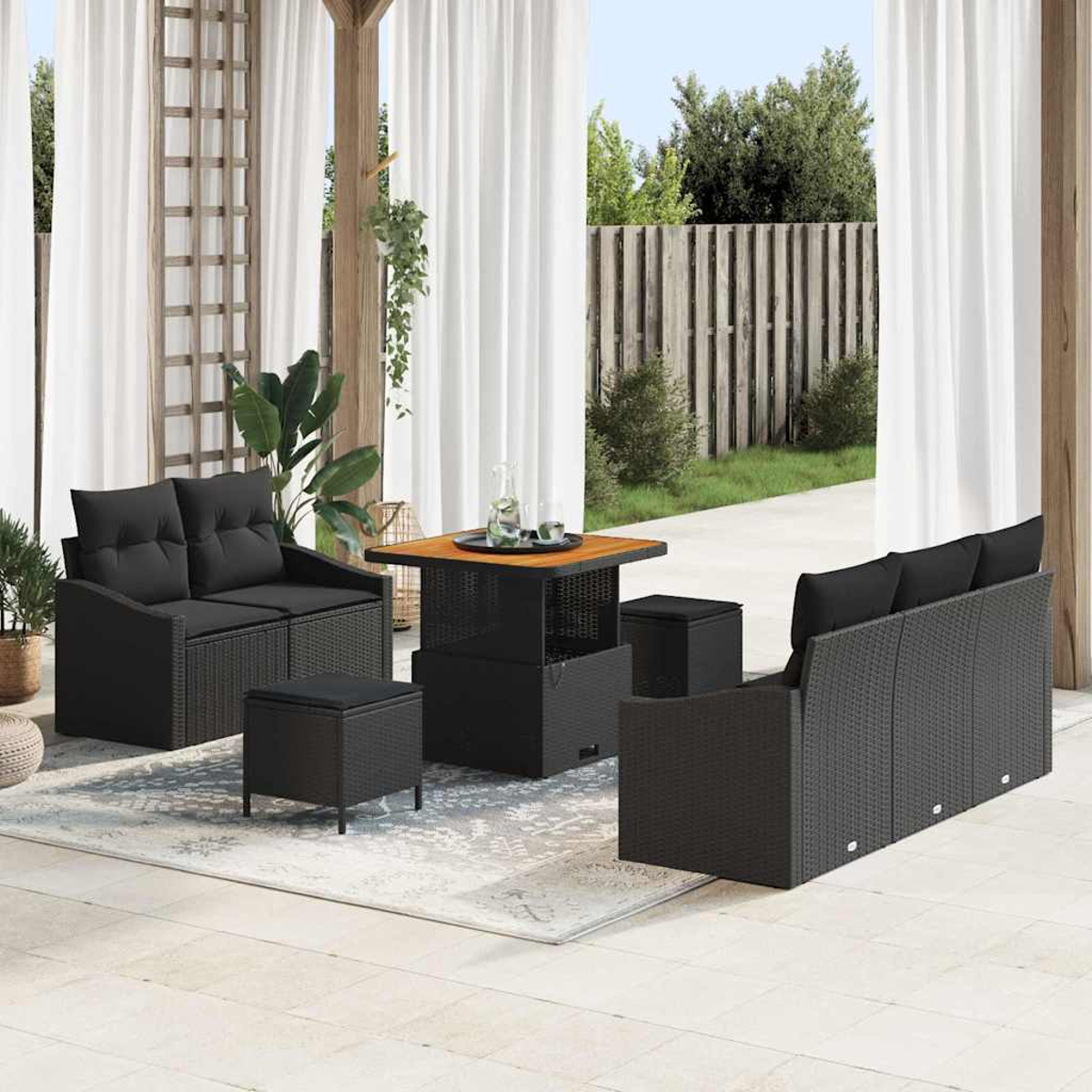 Terrassenset: schwarzes Rattan-Sofa, -Liebessitz, -Tisch und -Hocker. Weiße Vorhänge, grüne Pflanzen und Holzzaun im Hintergrund.