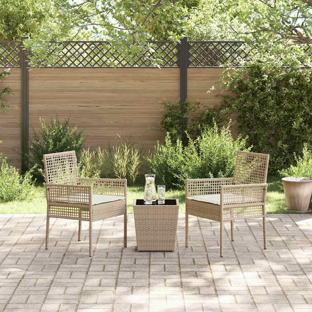 Terrasse im Freien mit zwei Korbstühlen, einem kleinen Tisch und Grün im Hintergrund.