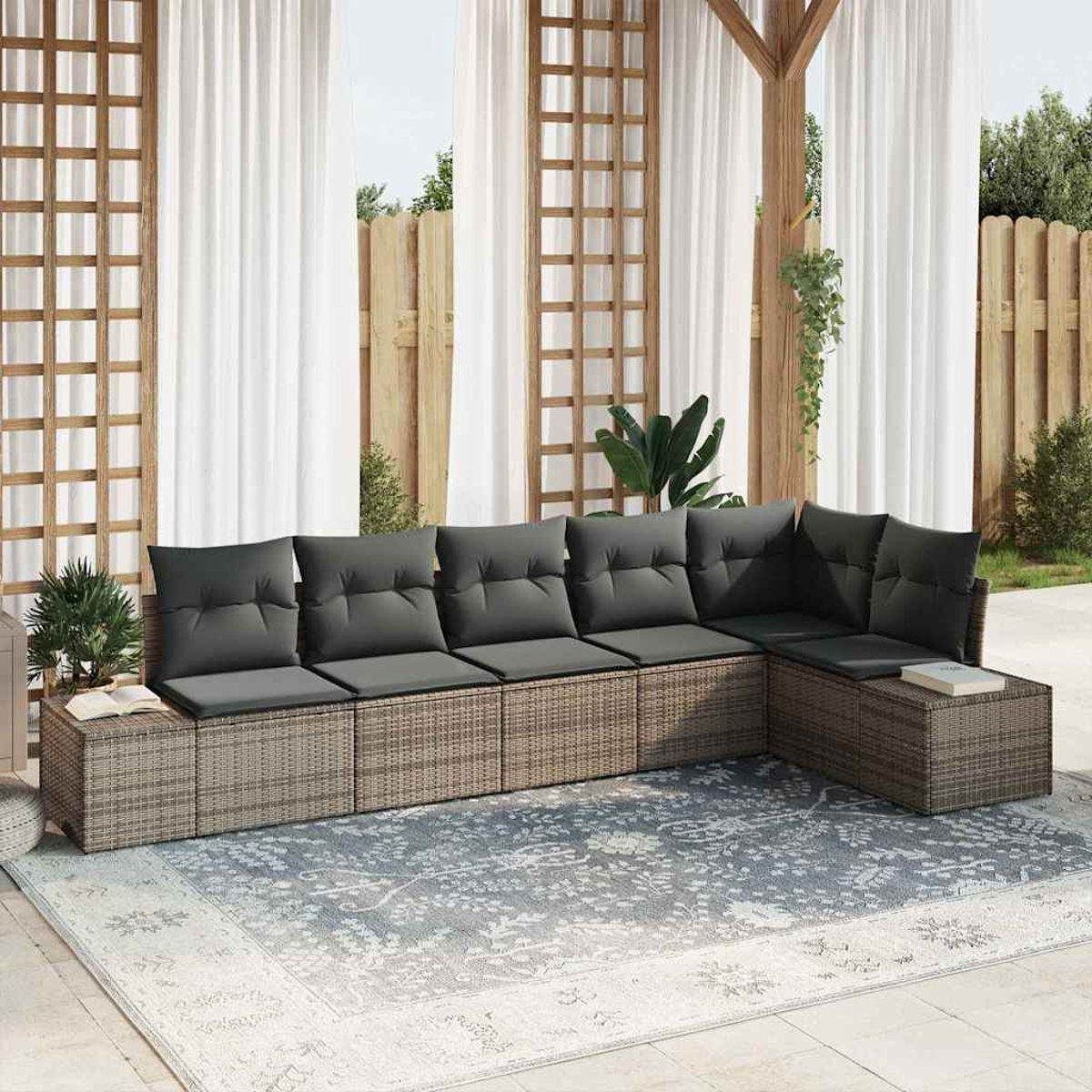Outdoor-Sitzbereich mit grauen Kissen, einem gemusterten Teppich und weißen Vorhängen. Holzkonstruktionen und Pflanzen sind sichtbar.