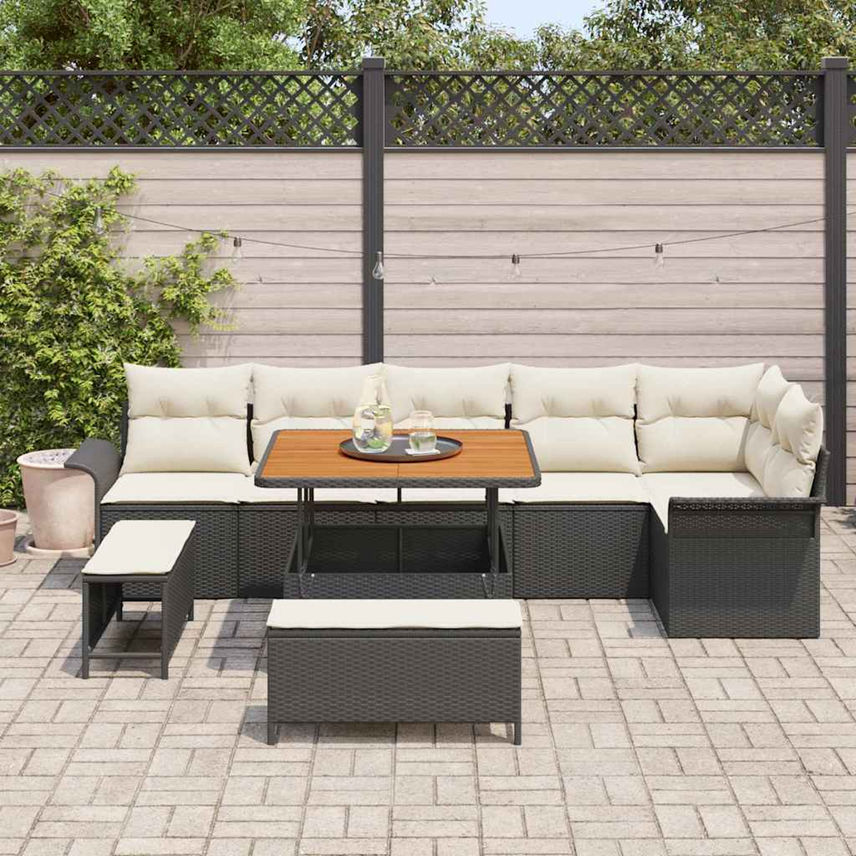 Outdoor-Ecksofa mit Kissen, Tisch mit Getränken, Bank und Aufbewahrungsbank auf einer Backstein-Terrasse. Zaun und Lichterkette im Hintergrund.