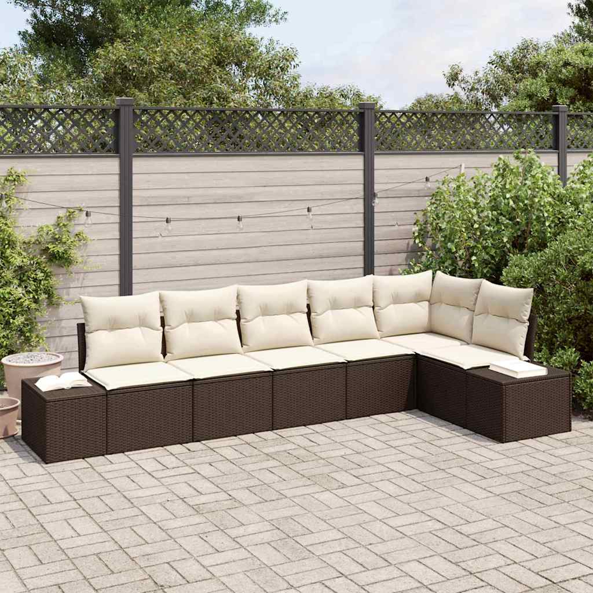 Ein Ecksofa mit cremefarbenen Kissen im Freien steht auf einer Backsteinterrasse. Im Hintergrund sind ein Zaun und Grün.
