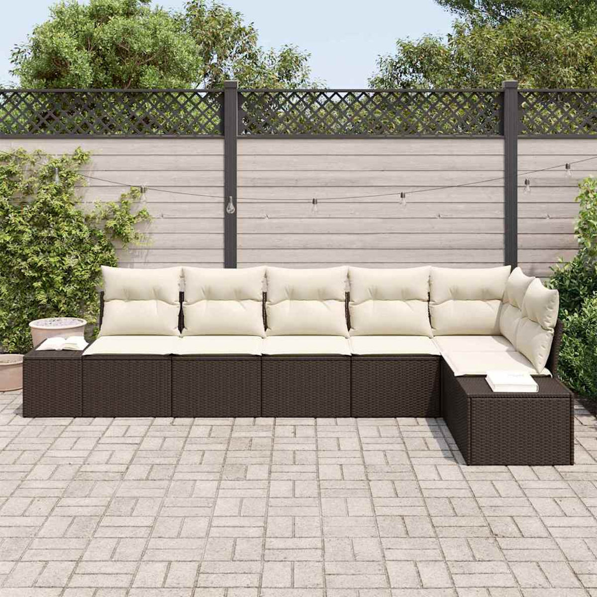 Ein Ecksofa im Freien mit beigen Kissen und braunem Korbbas, auf einer Steinterrasse mit Holzzaun im Hintergrund.