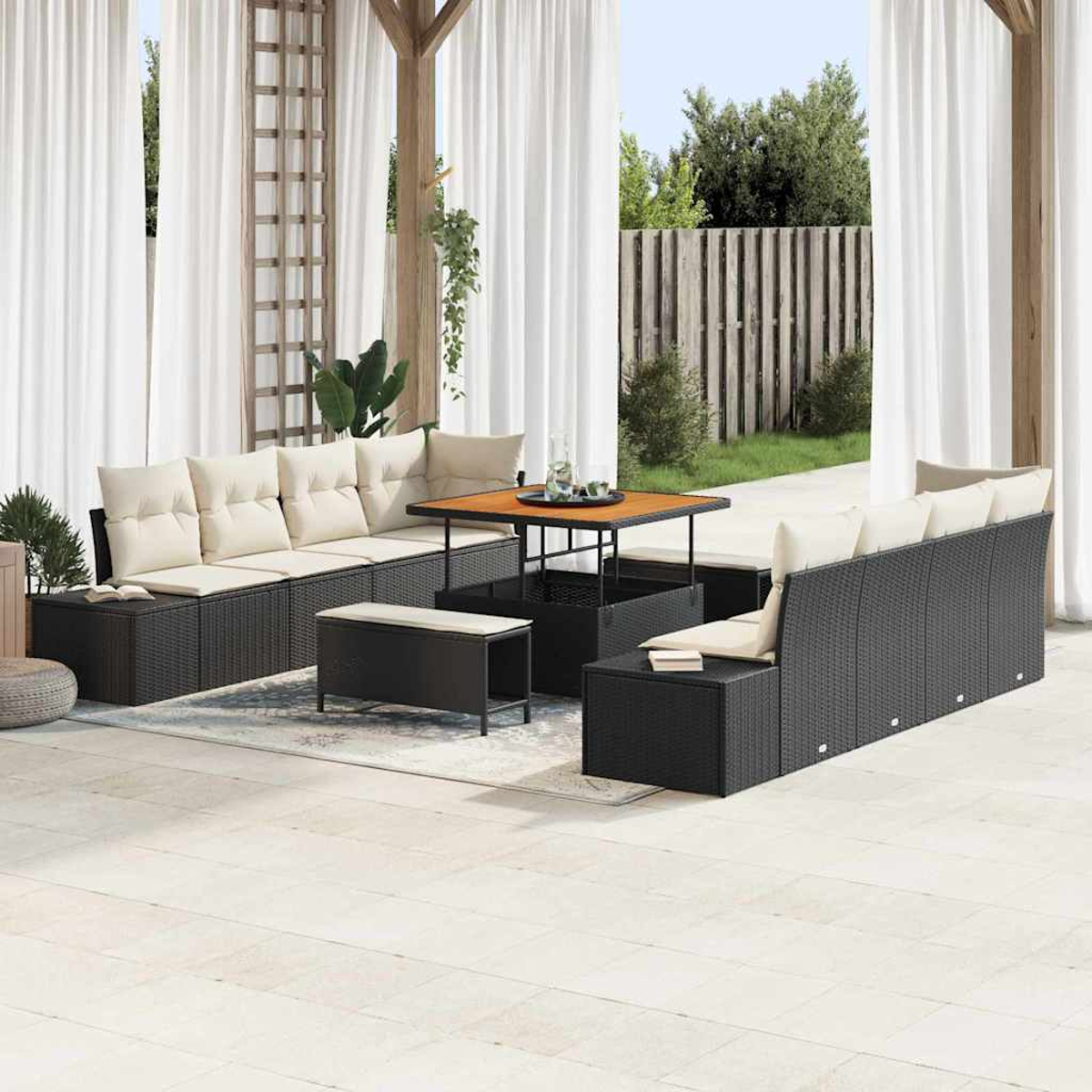 Outdoor-Terrassenset mit schwarzen Korbmöbeln, beigen Kissen, einem Holztisch und weißen Vorhängen. Grüne Pflanzen und ein Holzzaun im Hintergrund.