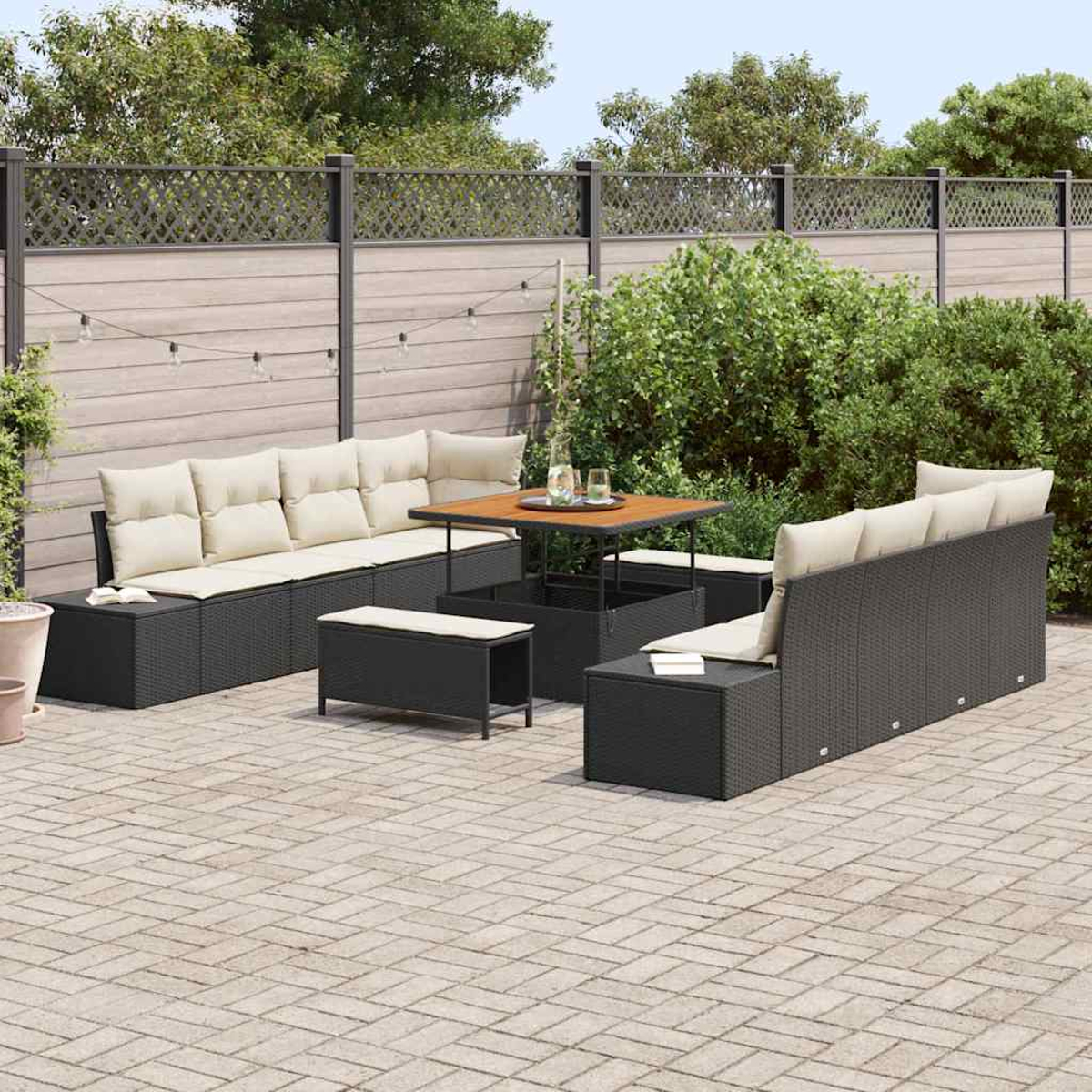 Gartenmöbel-Set: schwarze Korbsessel mit beigen Kissen, Holztisch und eine Backstein-Terrasse, mit Zaun und Grün.