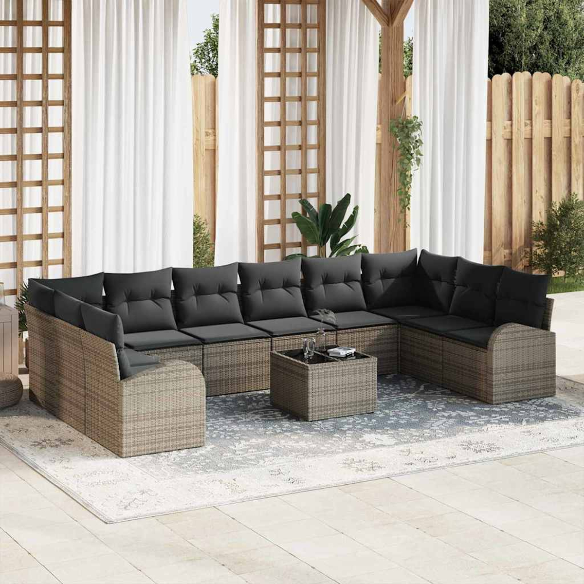 Außenbereich mit großem grauen Ecksofa, dunklen Kissen und kleinem Tisch auf einem gemusterten Teppich.