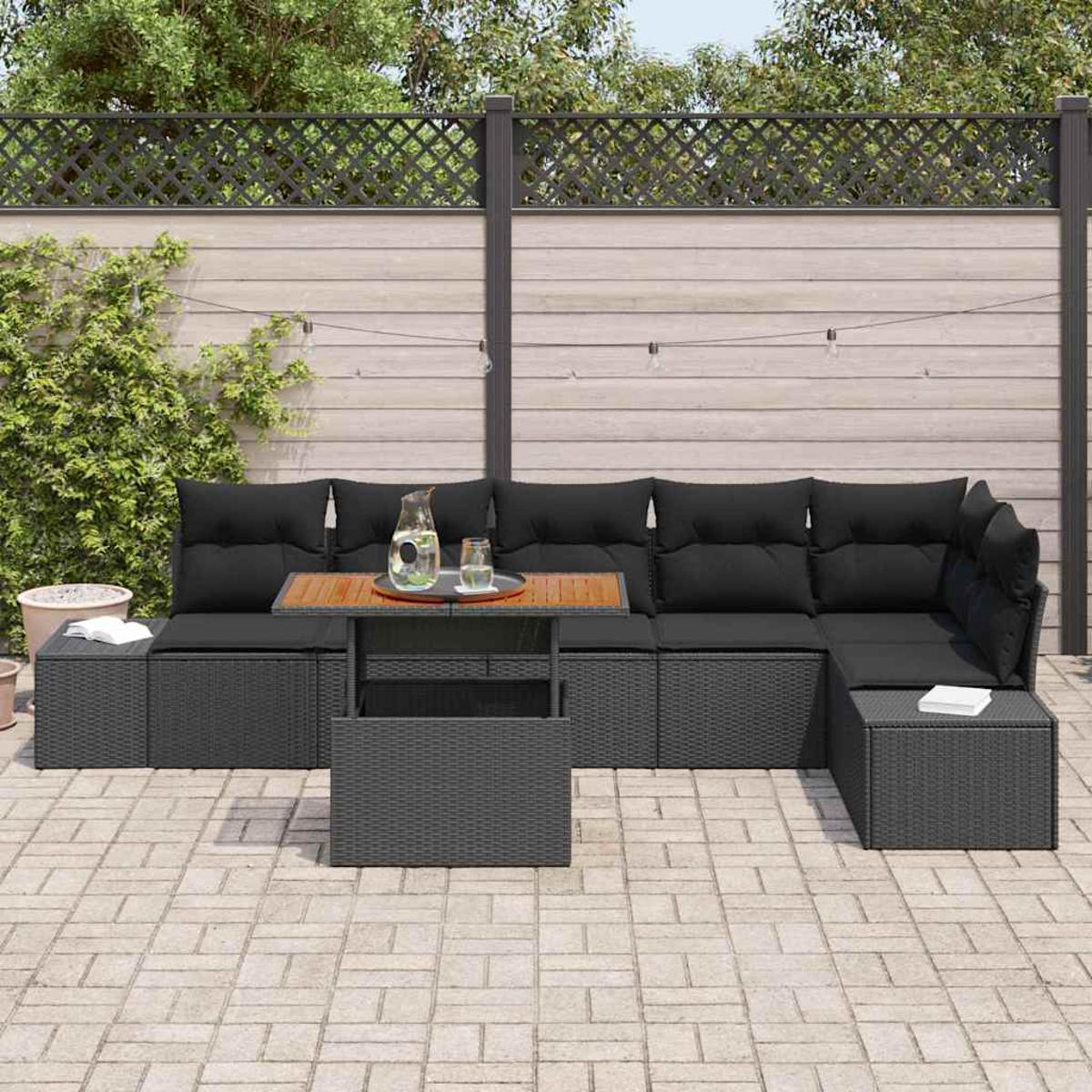 Outdoor-Ecksofa, schwarze Kissen, Holztisch mit Getränken, graue Terrasse, Holzzaun und grüne Pflanzen.