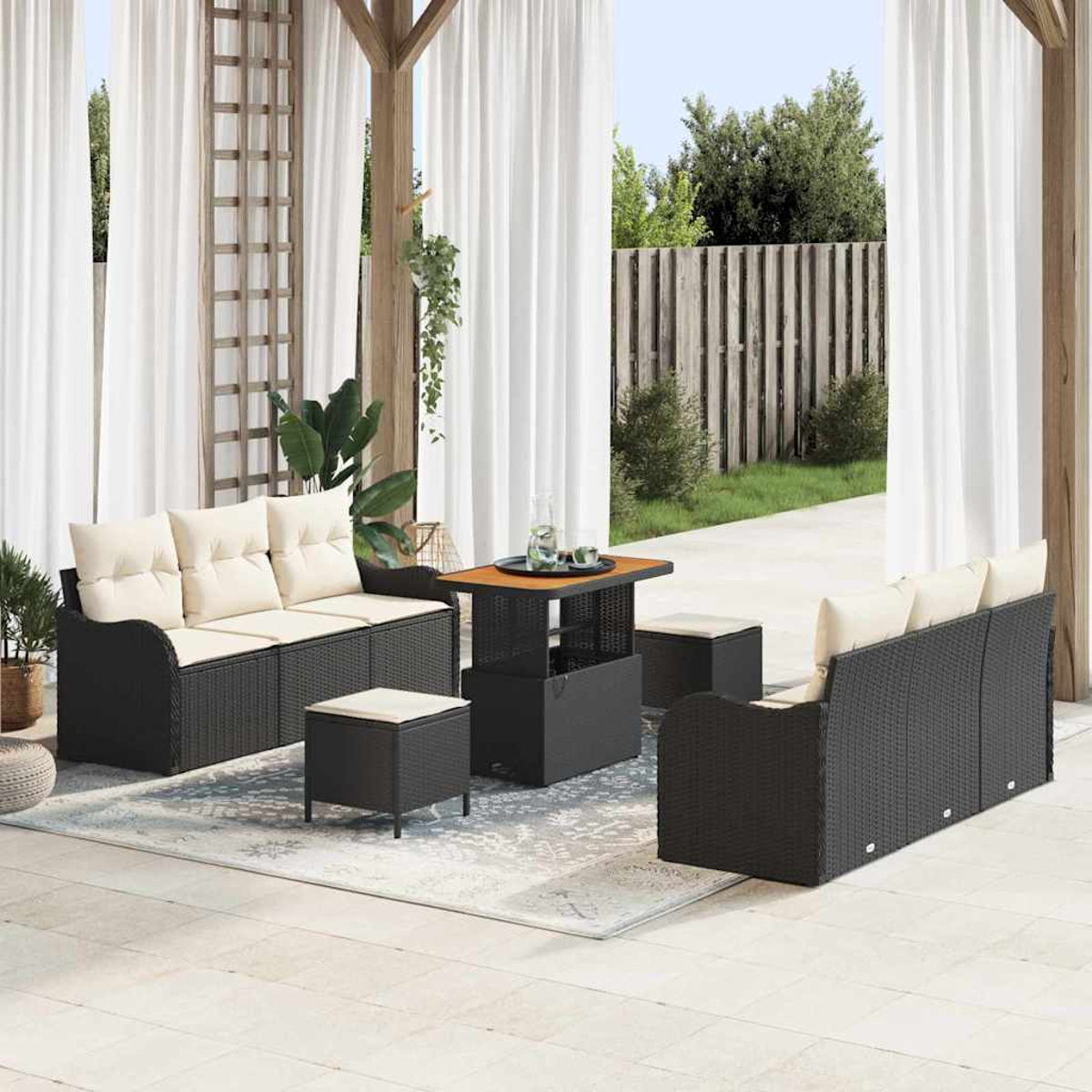 Außenbereich mit schwarzen Korbmöbeln, cremefarbenen Kissen und einem Holztisch. Transparente weiße Vorhänge umrahmen den Gartenblick.
