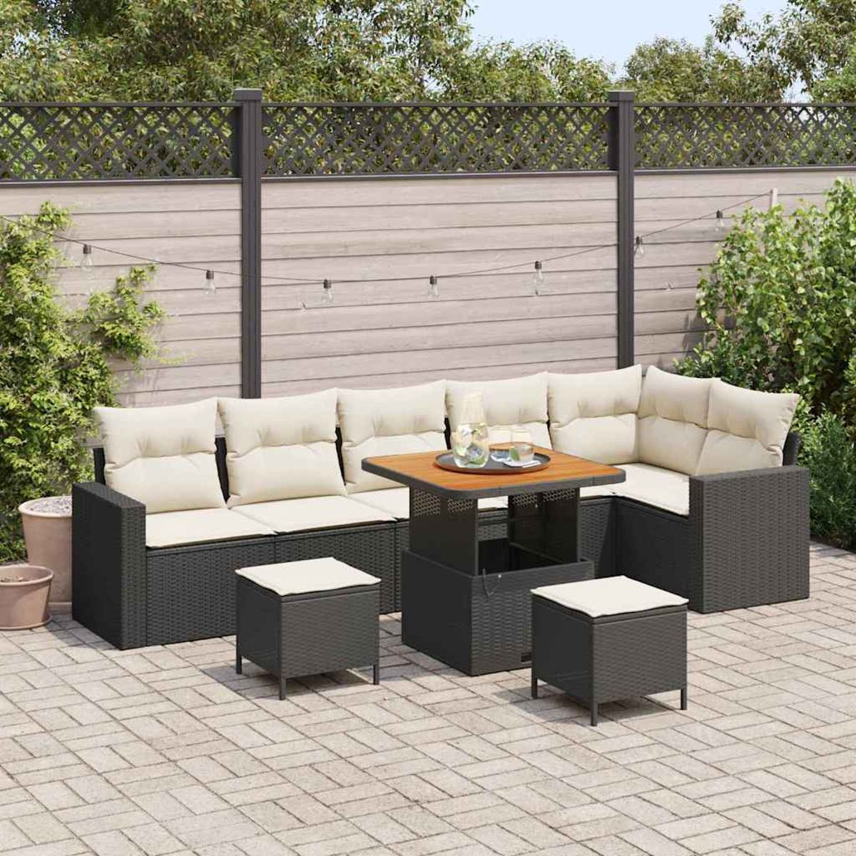 Outdoor-Sitzgruppe mit Ecksofa, zwei Ottomanen und einem Tisch. Beige Kissen, dunkelgraue Rahmen, auf einer Backstein-Terrasse. Zaun im Hintergrund.