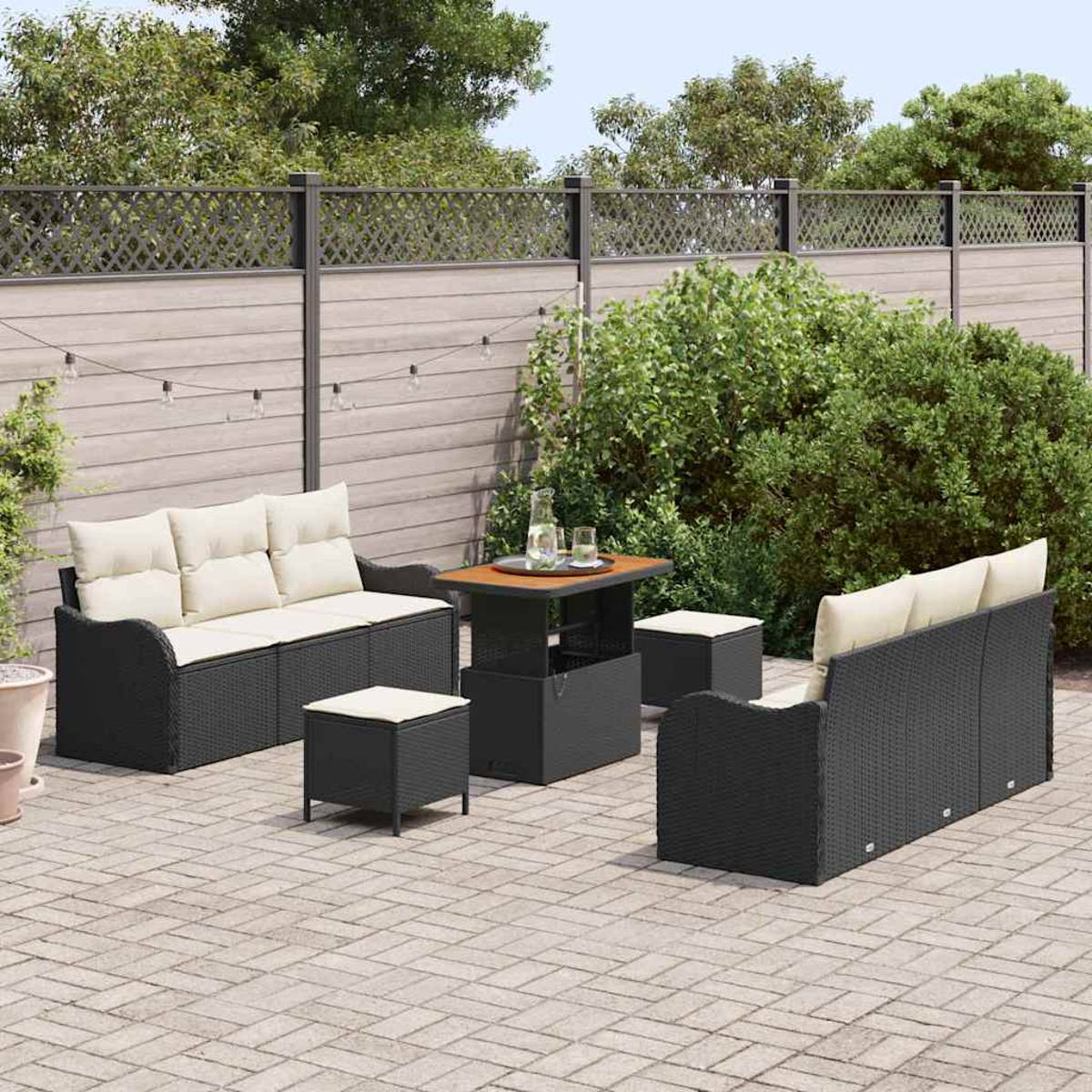 Gartenmöbel-Set: schwarze Korbsessel, Ottomane und Tisch mit beigen Kissen auf einer Ziegelterrasse, in der Nähe eines Holzzauns.