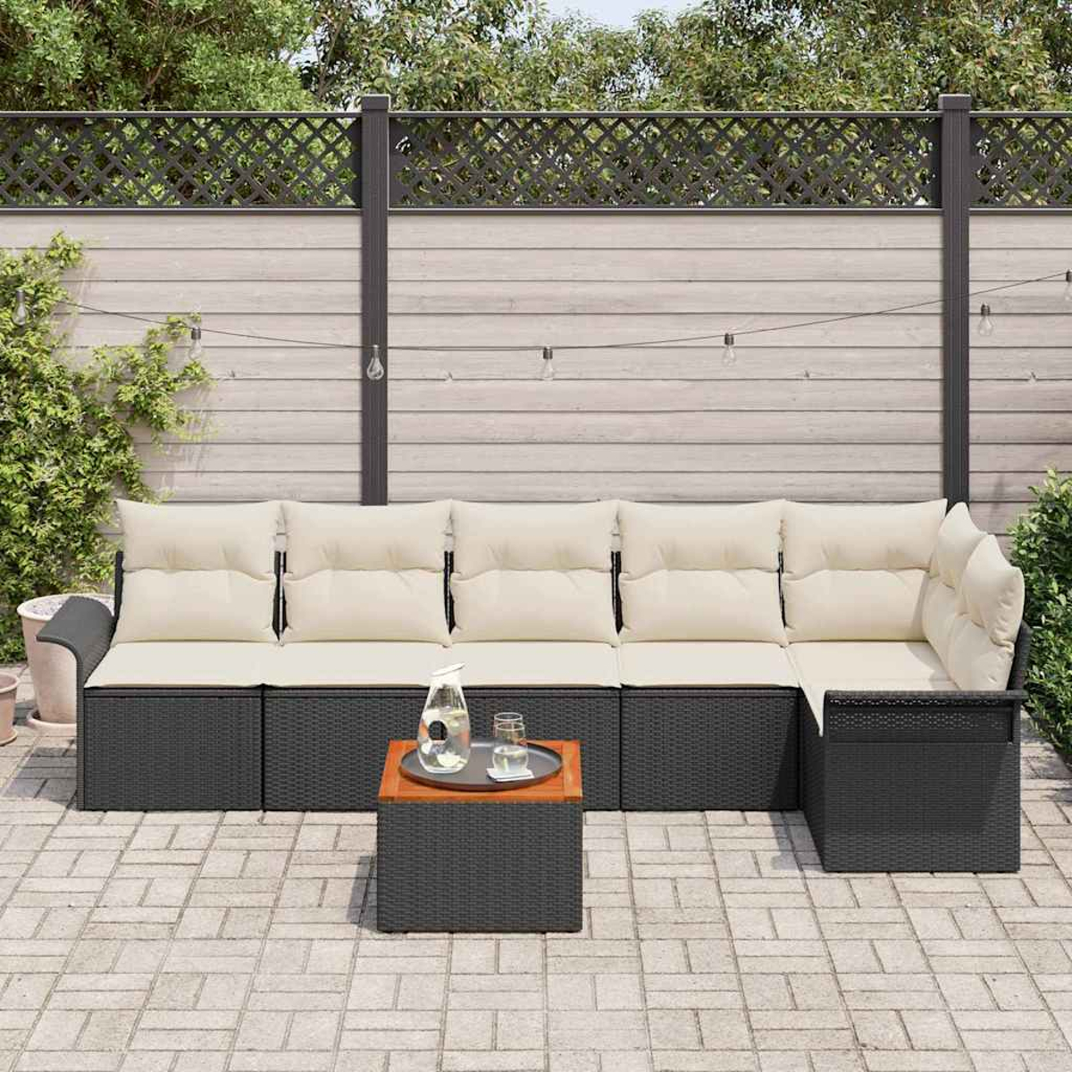 Outdoor-Ecksofa mit cremefarbenen Kissen, kleiner Tisch mit Getränken, auf der Terrasse. Holzzaun und Grün im Hintergrund.
