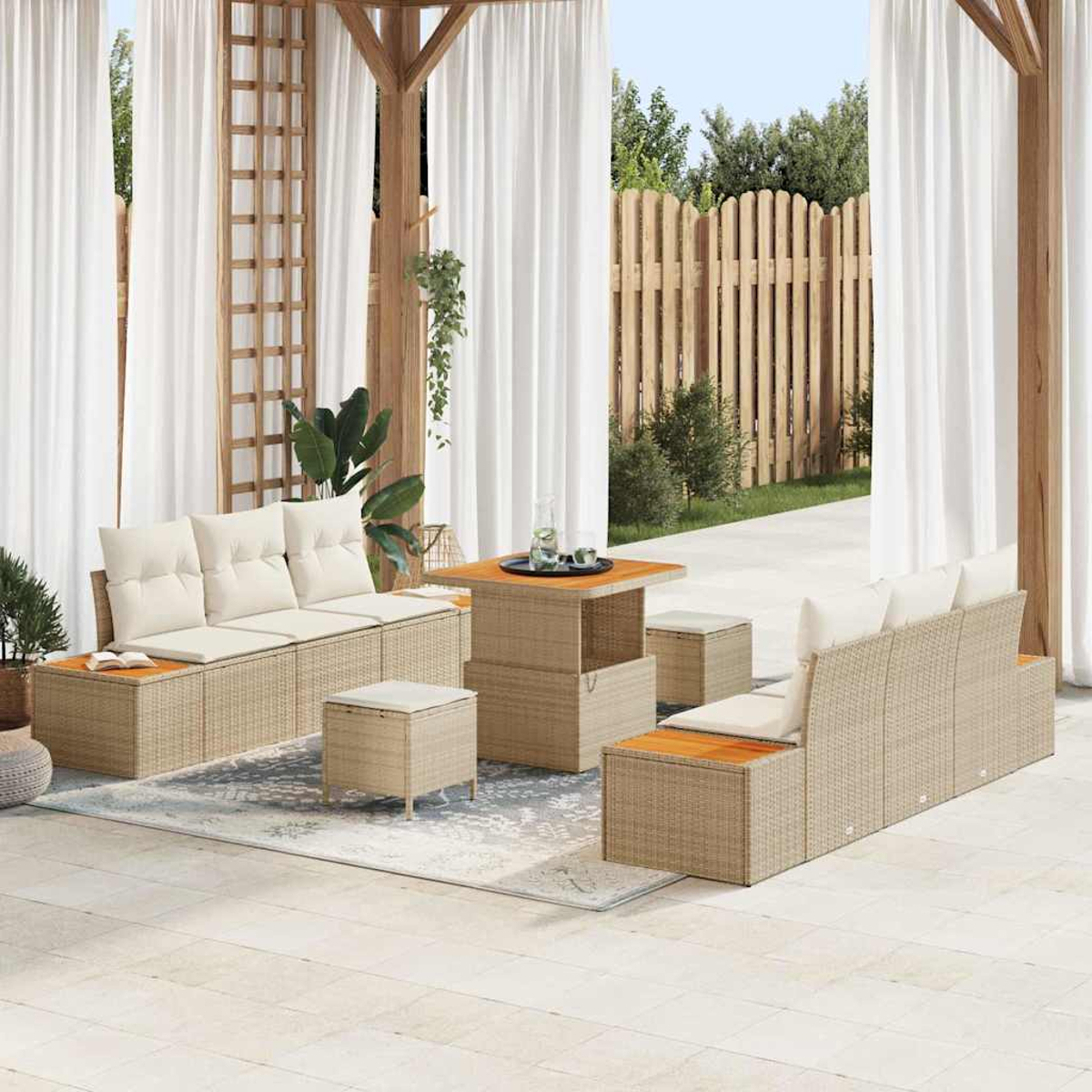 Ein Terrassenset im Freien. Beige gewebte Sofas mit cremefarbenen Kissen, ein Tisch und Hocker stehen auf einem hellen Teppich. Weiße Vorhänge und ein Zaun sind im Hintergrund.