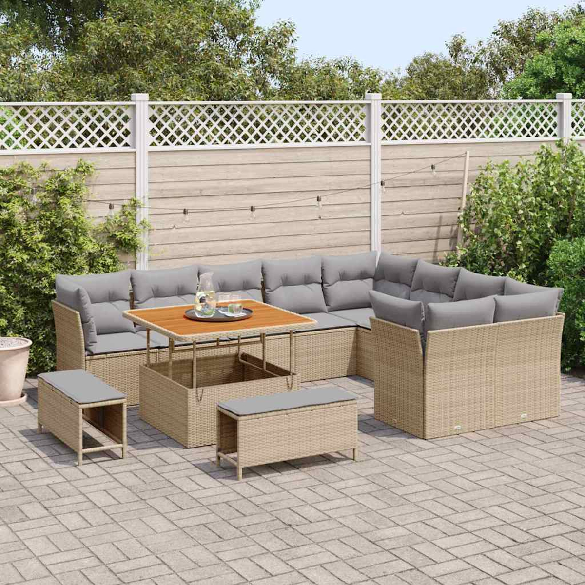 Gartenmöbel-Set. Beige Korbsessel mit grauen Kissen, Holztisch. Auf einer Backstein-Terrasse mit weißem Zaun und Grün.