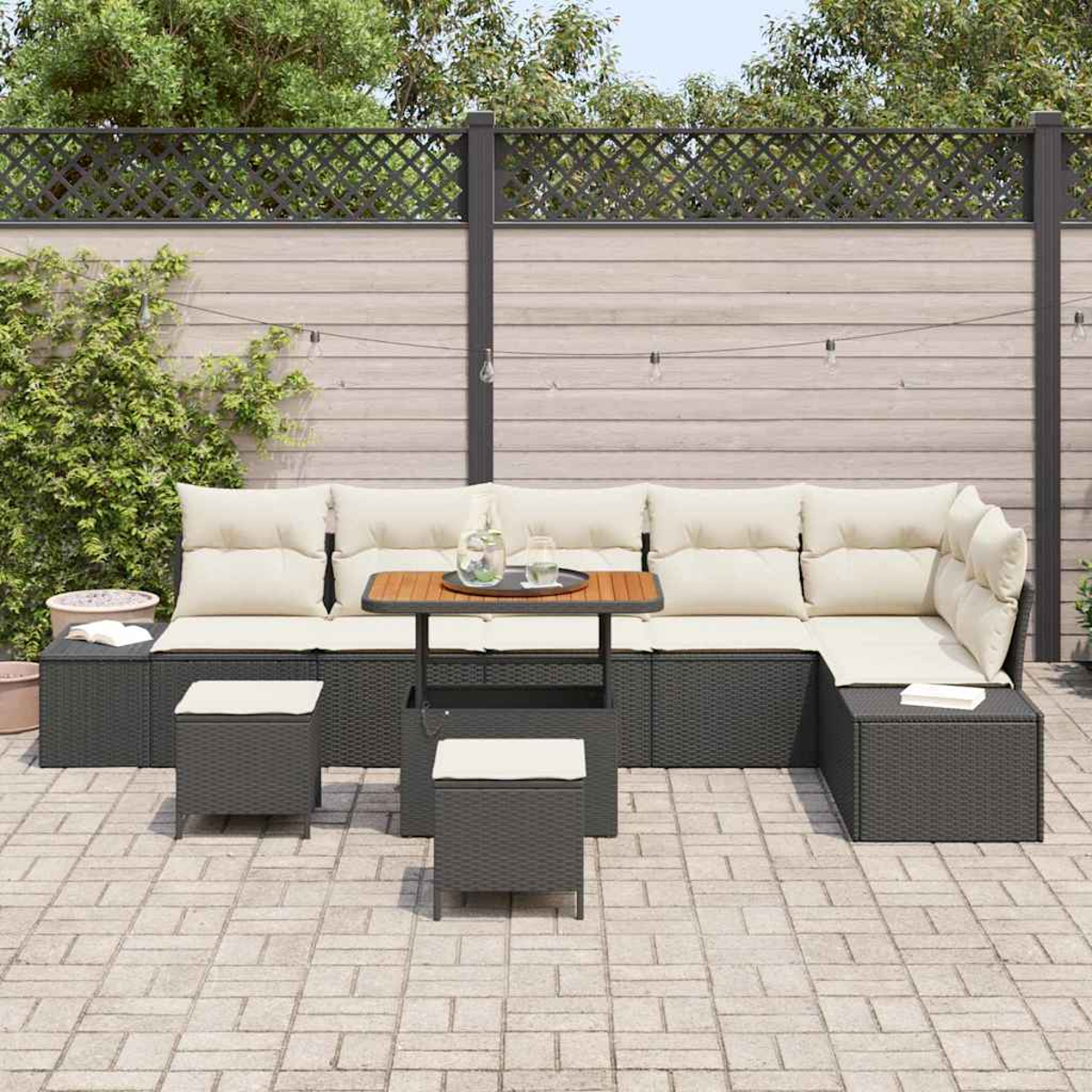 Garten-Terrassenset mit Ecksofa, kleinem Tisch und zwei Hockern. Beige Kissen, dunkelgraue Möbel und Holzzaun.