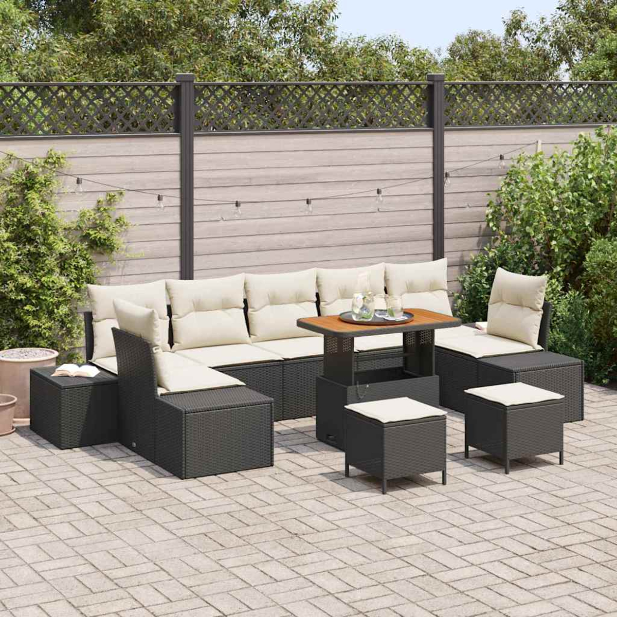 Garten-Sitzgruppe. Dunkle Korbmöbel mit cremefarbenen Kissen. Tisch mit Holzplatte, umgeben von Hockern, auf einer Steinpflasterung.