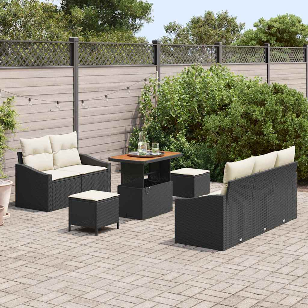 Garten-Terrassenset mit schwarzen Korbmöbeln, beigen Kissen und einem Holztisch. Auf einer Backstein-Terrasse mit Holzzaun und Grün.