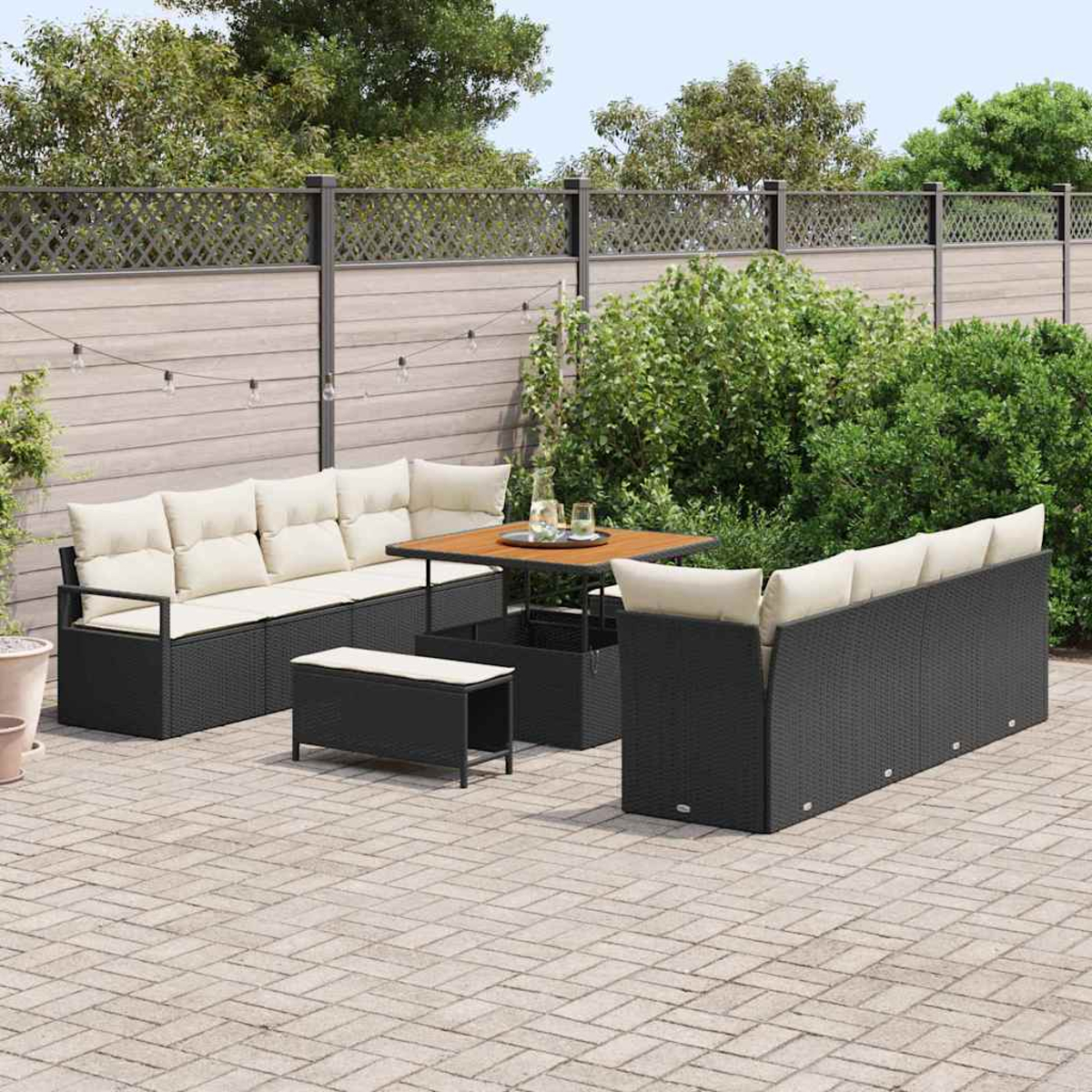 Juego de patio con muebles de mimbre negro, cojines beige, mesa de madera y banco a juego sobre adoquines de piedra.