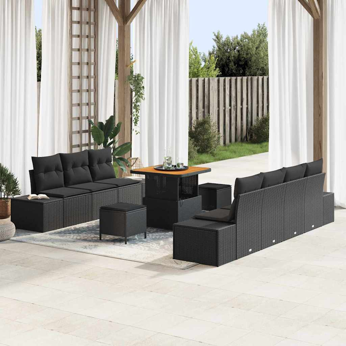 Gartenmöbel-Set mit schwarzen Korbsitzgruppen, Ottomanen und einem Tisch unter einer Holzpergola mit weißen Vorhängen.
