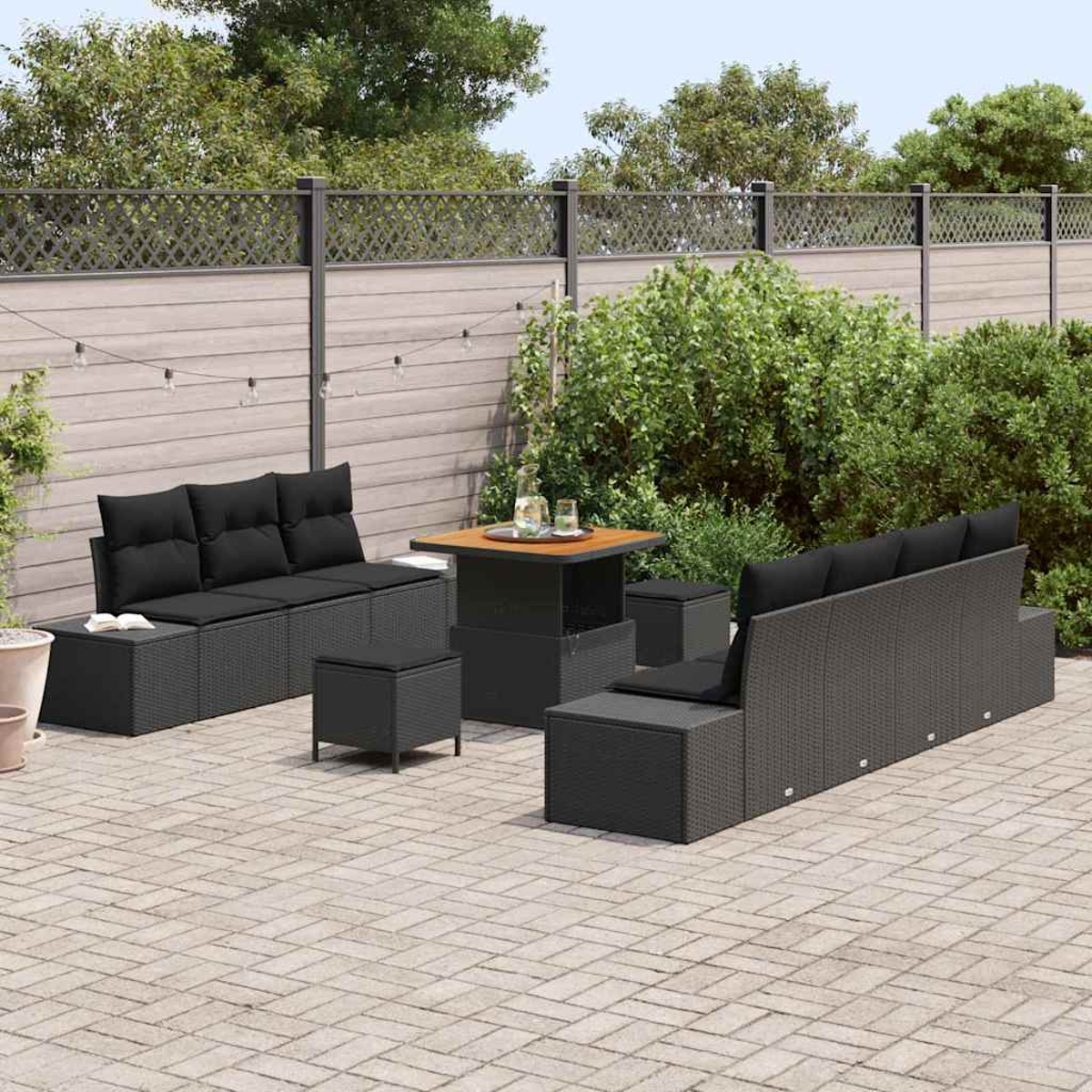 Garten-Terrassenset mit schwarzen Kissen. Ein Tisch und Sitzbereich. Hinter dem Set befinden sich ein Holzzaun und grüne Büsche.