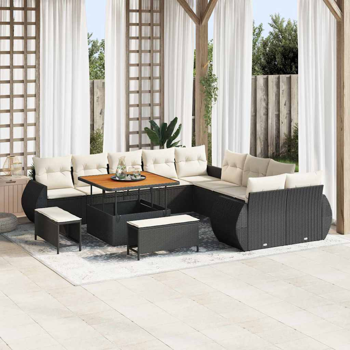 Terrassenset mit schwarzen Korbmöbeln, beigen Kissen, Holztisch und weißen Vorhängen im Hintergrund. Auf dem Boden liegt ein Teppich.