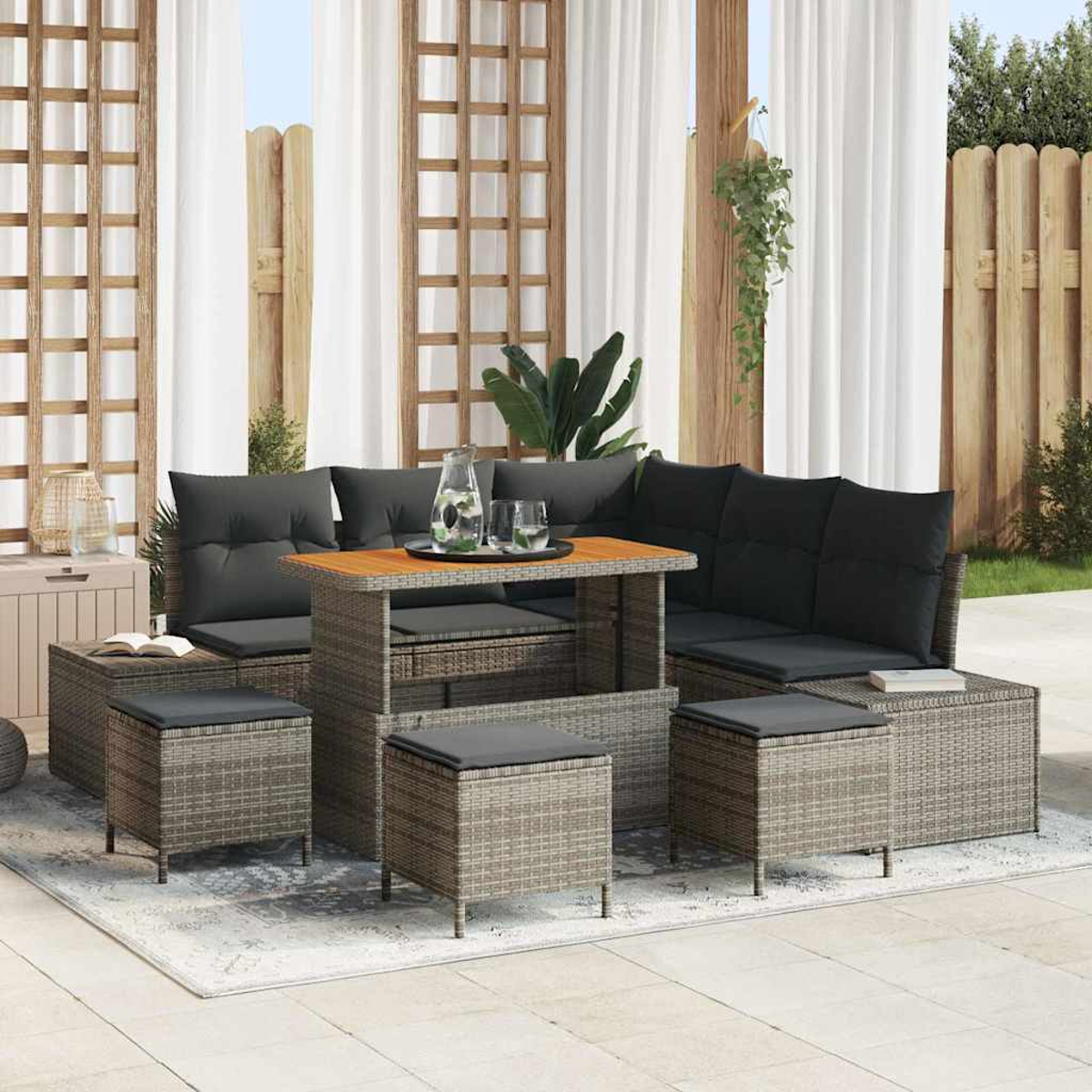 Outdoor-Sitzgruppe mit grauen Kissen, einem Holztisch und Hockern. Vorhänge und ein Zaun sind im Hintergrund.