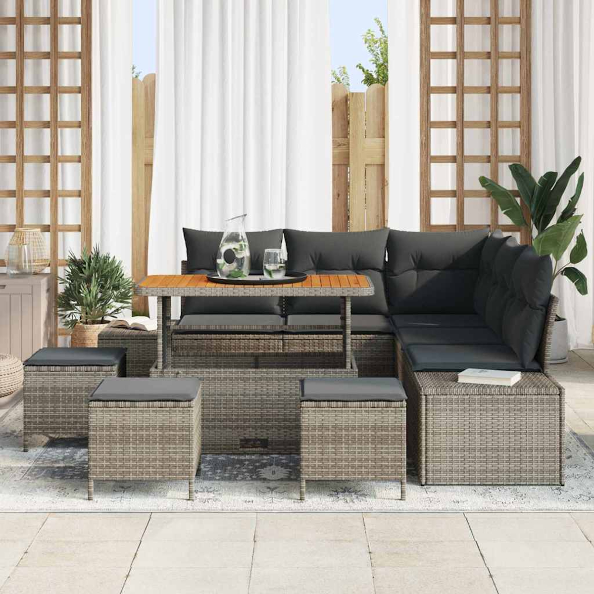 Terrassenset mit Sofa, Tisch und Hockern. Graue Kissen und Korbmöbel. Weiße Vorhänge und Holzgitter.