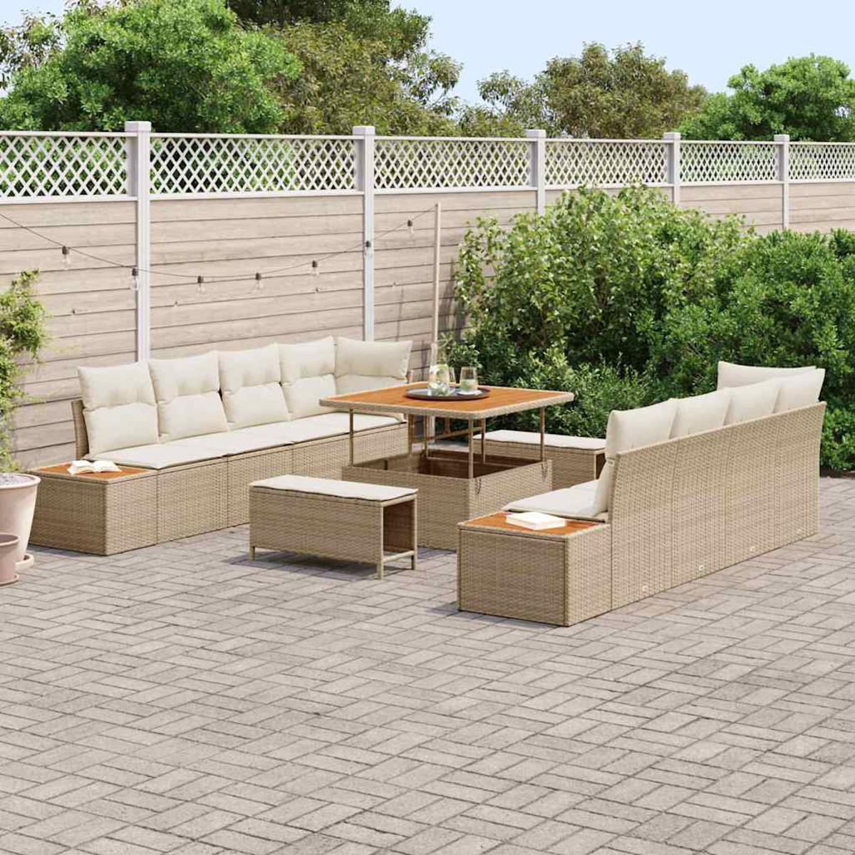 Garten-Sitzgruppe auf einer Terrasse. Besteht aus einem Sofa, Tisch und Bänken. Im Hintergrund ein weißer Zaun und Grün.