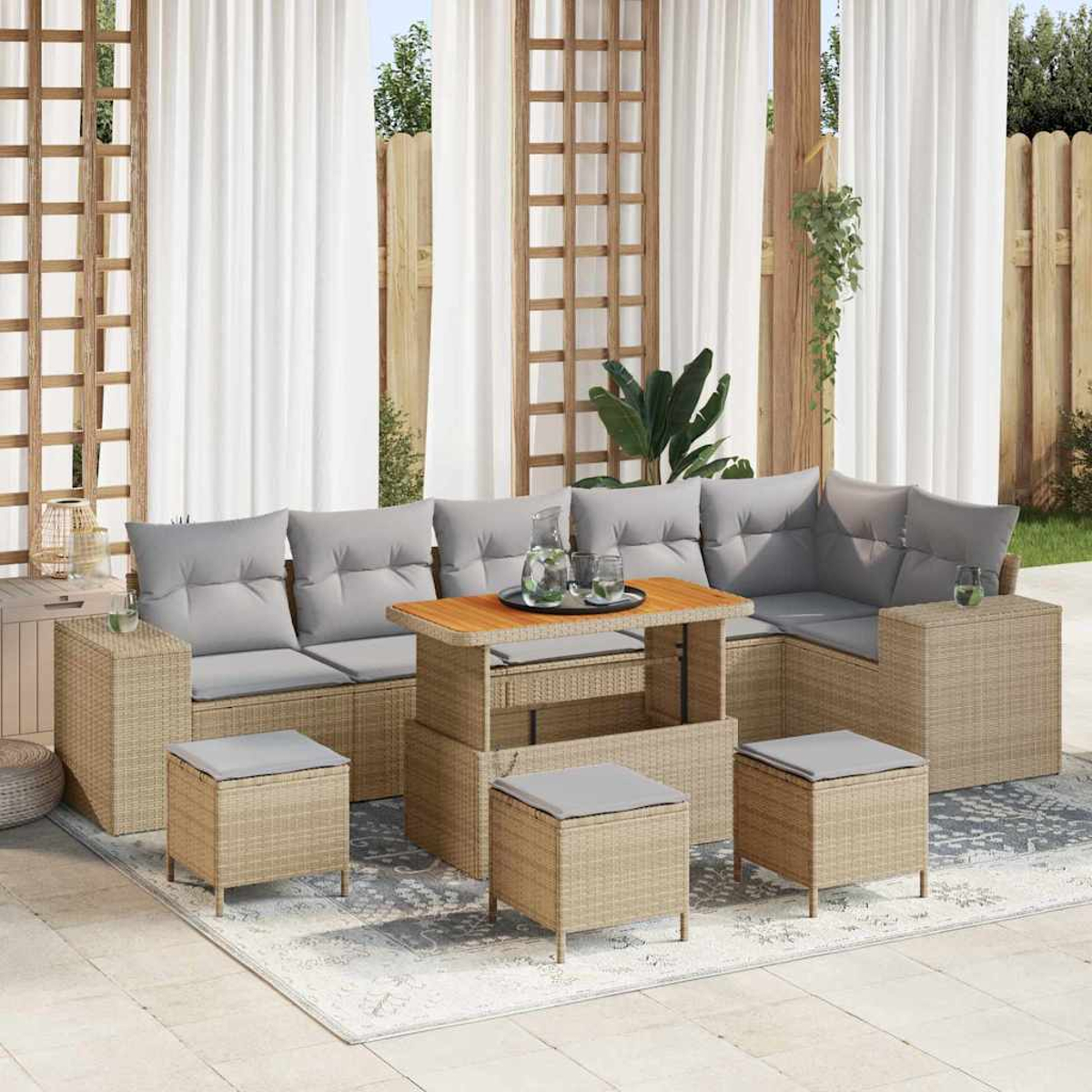 Rattan-Sofa-Set für den Außenbereich mit grauen Kissen und Holztisch. Inklusive Ottomanen und Beistelltischen, auf einem gemusterten Teppich, in der Nähe von Vorhängen.