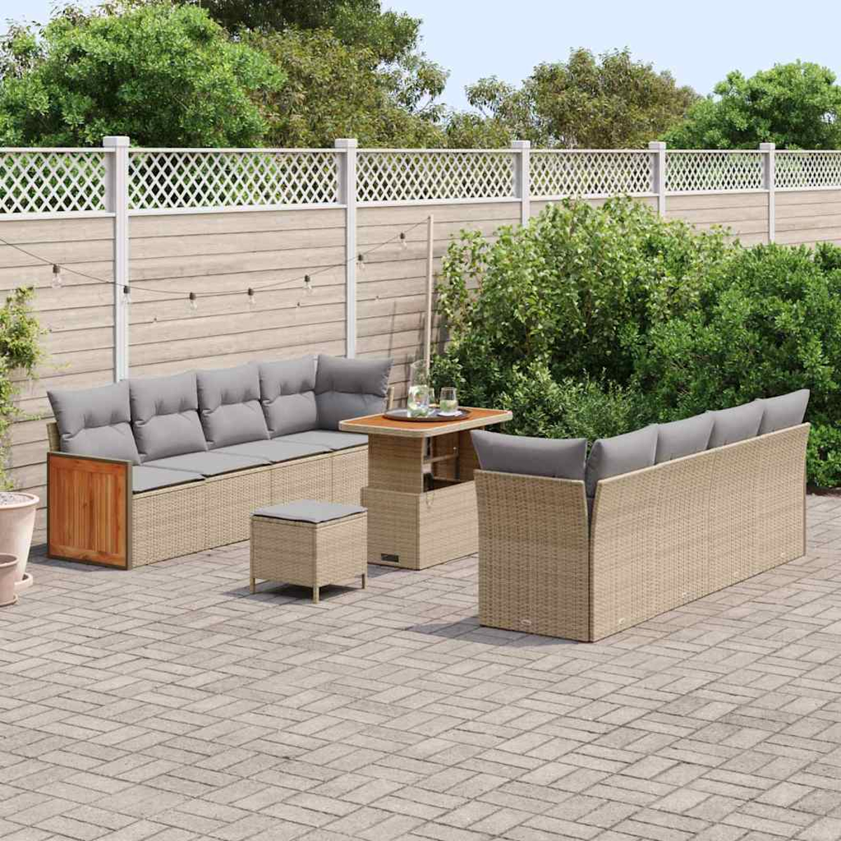 Garten-Terrassenset mit Korbmöbeln, einem Tisch und einem kleinen Hocker auf einer Ziegelterrasse, mit weißem Zaun und grünem Laub im Hintergrund.