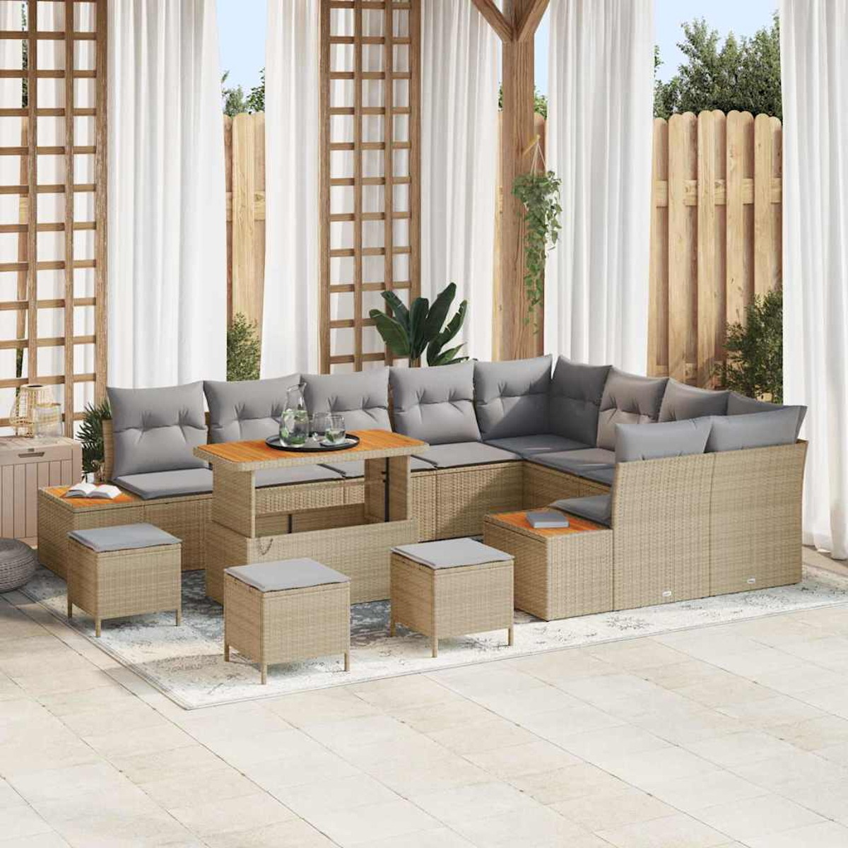Outdoor-Ecksofa mit grauen Kissen, Couchtisch und Hockern auf einem Teppich. Weiße Vorhänge und Holzzaun im Hintergrund.