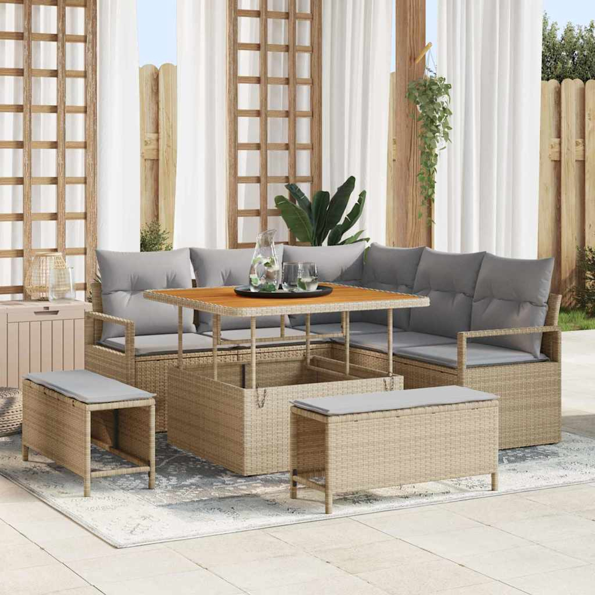 Terrassenset: Korbmöbel, Tisch und Bänke mit grauen Kissen. Holzzaun, weiße Vorhänge und Pflanzen im Hintergrund.