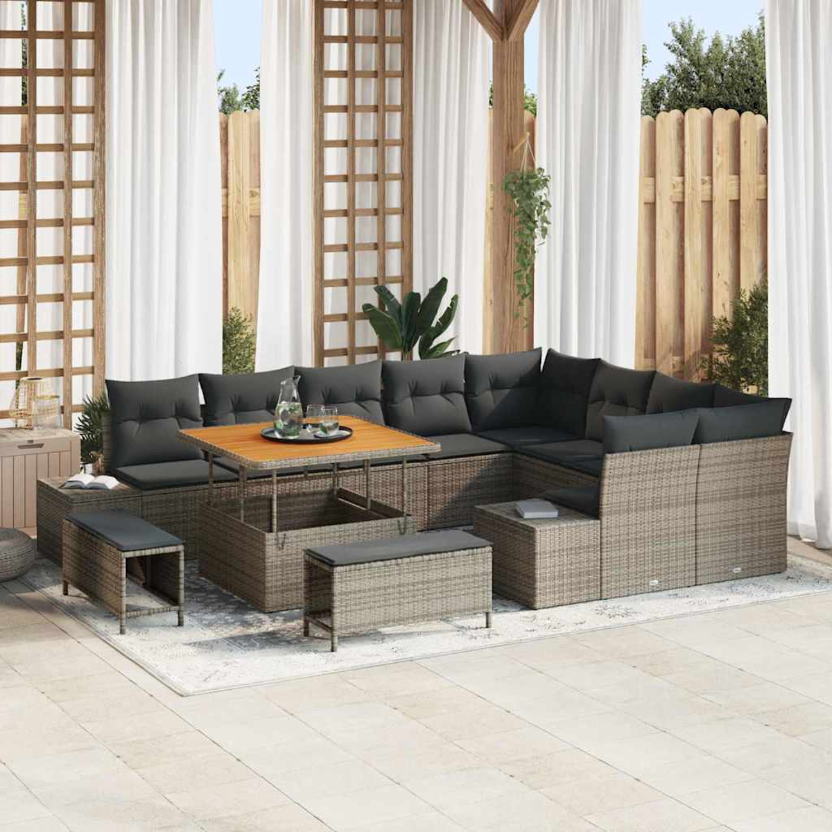 Terrassenset mit grauen Kissen, Holztisch und Bänken. Weiße Vorhänge und Holzzaun im Hintergrund.