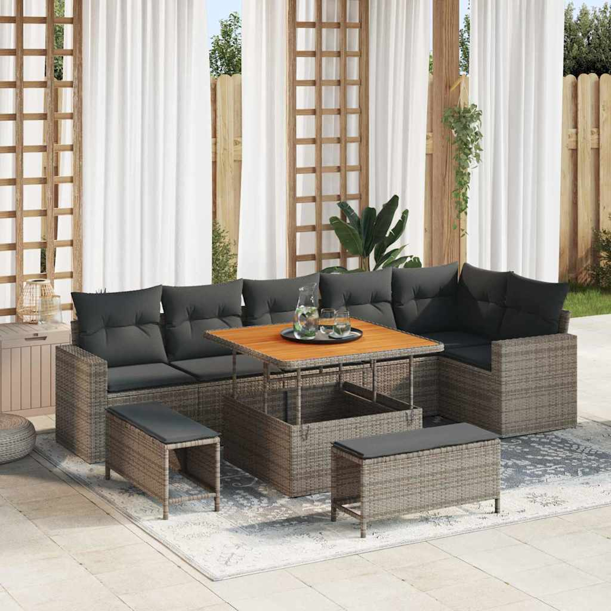 Rattan-Sofa-Set im Freien mit grauen Kissen und einem Holztisch. Weiße Vorhänge und ein Holzzaun im Hintergrund.
