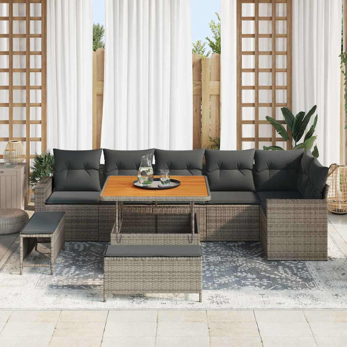 Graues Outdoor-Geflechtsofa mit dunklen Kissen, Holztisch und einer Bank. Vorhänge und ein Spalier sind im Hintergrund.