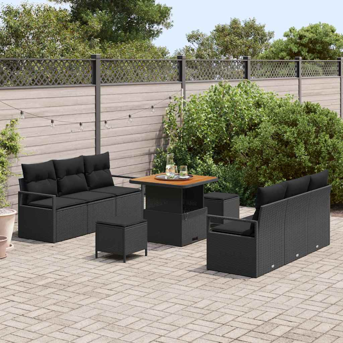 Garten-Terrassenset mit schwarzen Korbmöbeln, einem quadratischen Tisch und einem Holzzaun. Grüne Büsche und Bäume im Hintergrund.