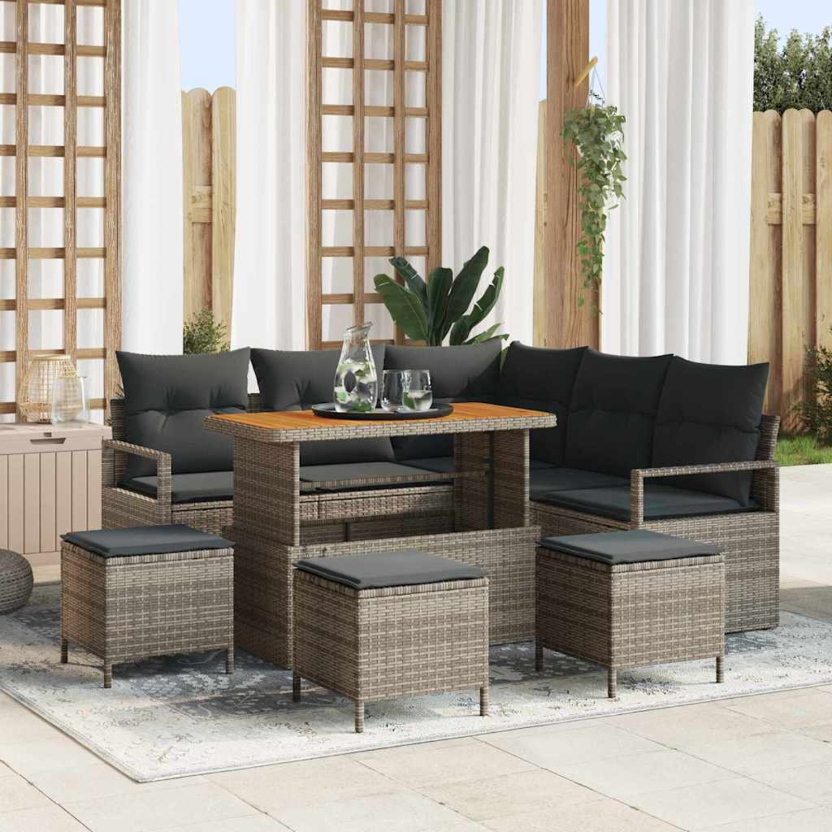 Gartenmöbel-Set aus Rattan mit Tisch, Sofa und Hockern. Enthält Kissen und eine Glaskanne, alles auf einem Teppich und Terrassenbereich.