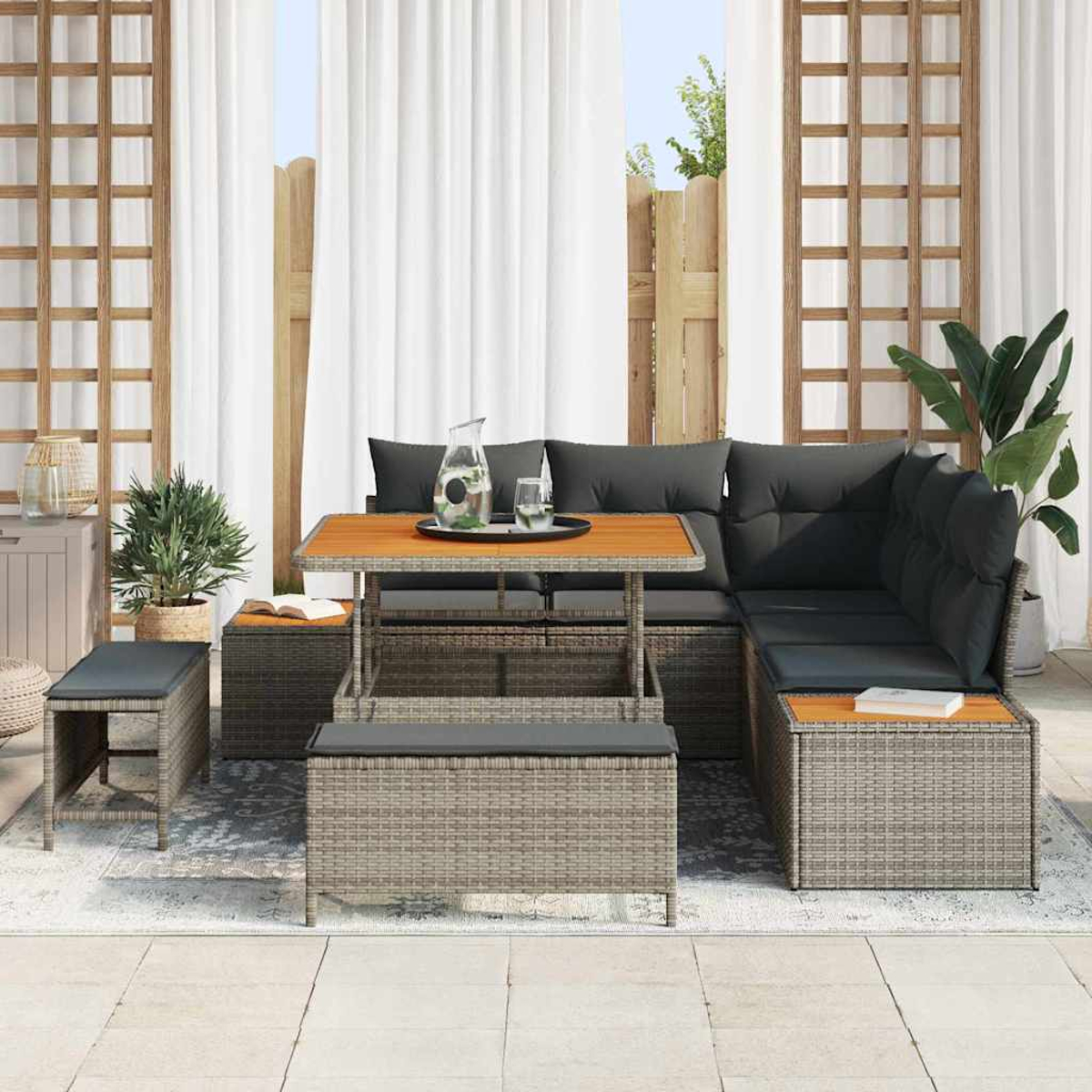 Outdoor-Ecksofa mit Holztisch, Kissen und kleinem Hocker. Auf dem Tisch stehen ein Krug und Gläser, im Hintergrund weiße Vorhänge.