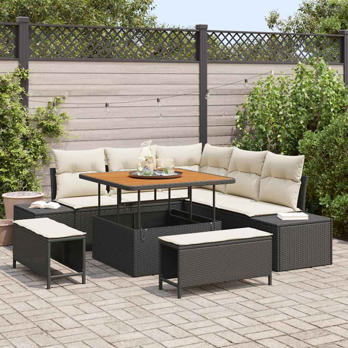 Garten-Terrassenset mit schwarzer Korbmöbeln, beigen Kissen und einem Holztisch. Im Hintergrund ein Zaun und Pflanzen.