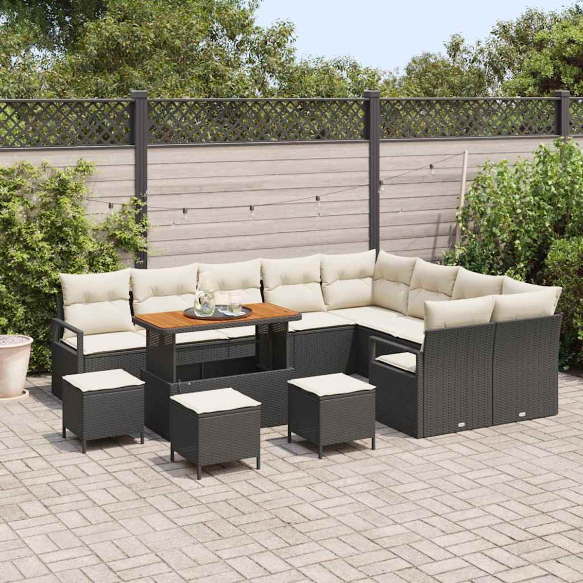 Gartenmöbel-Set auf einer Terrasse. Es umfasst ein Ecksofa mit beigefarbenen Kissen, einen Tisch und mehrere Hocker. Im Hintergrund ein Zaun.