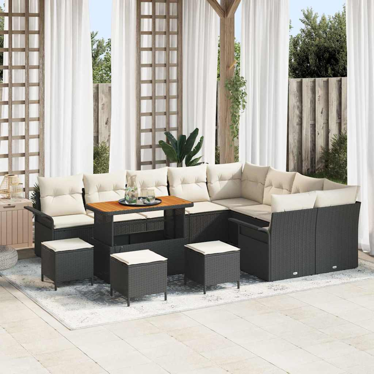 Terrassenmöbel-Set im Freien: dunkles Korbmöbelsofa mit cremefarbenen Kissen, Holztisch und Hockern. Weiße Vorhänge im Hintergrund.