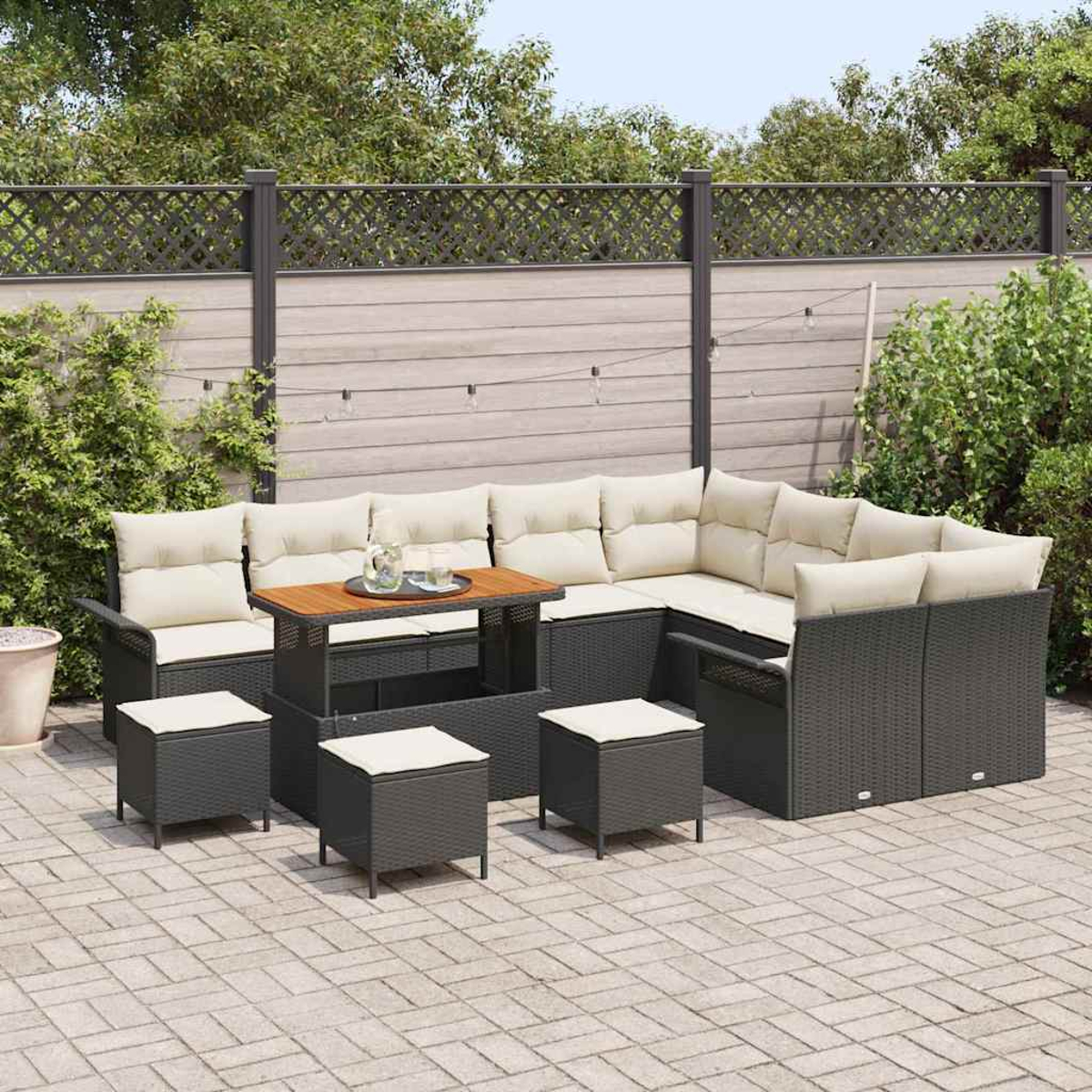 Outdoor-Ecksofa mit beigen Kissen, Holztisch mit Gläsern und vier kleinen Hockern. Im Hintergrund sind ein Zaun und Bäume zu sehen.