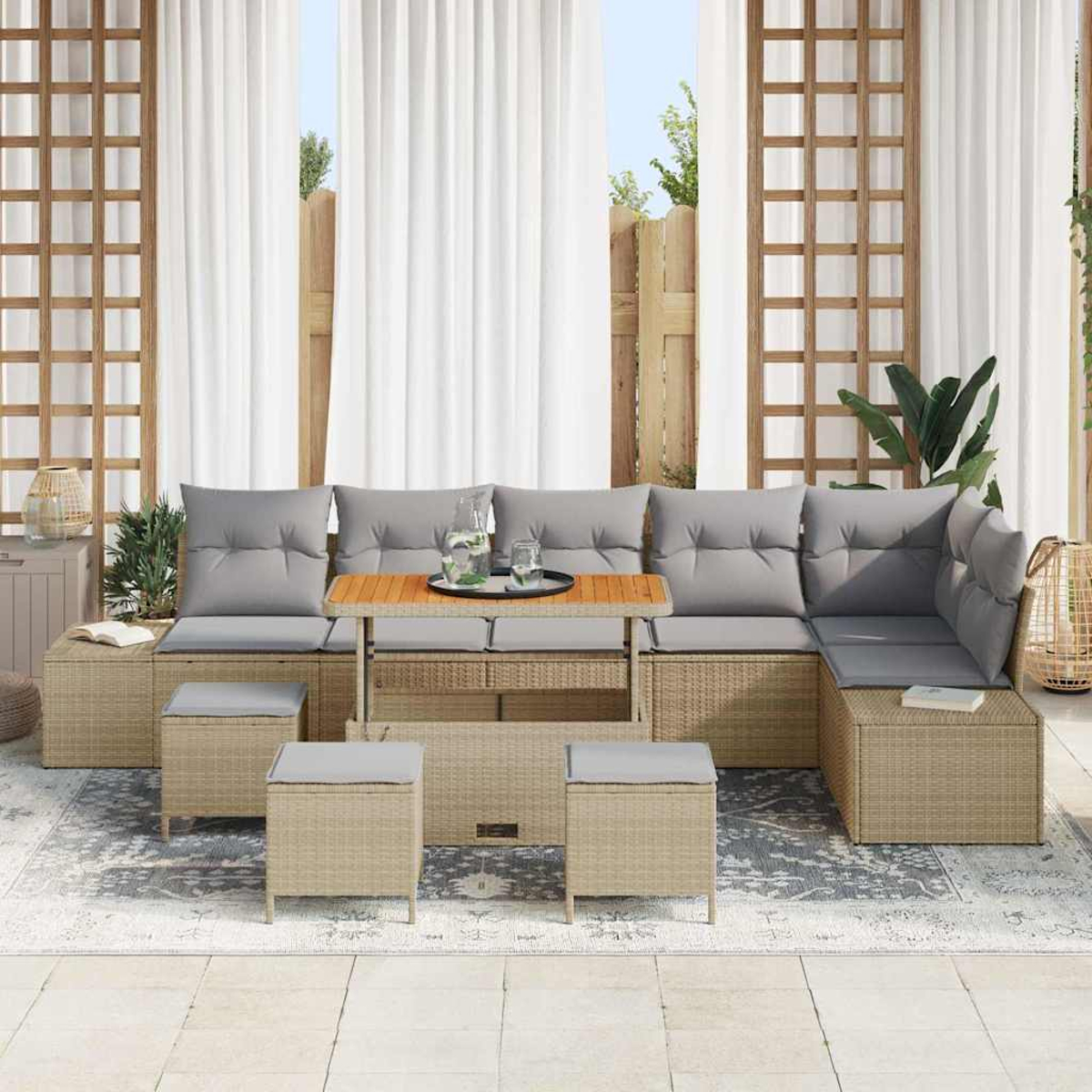 Outdoor-Korbmöbel-Set mit grauen Kissen und einem Holztisch. Weiße Vorhänge und Spalier im Hintergrund.