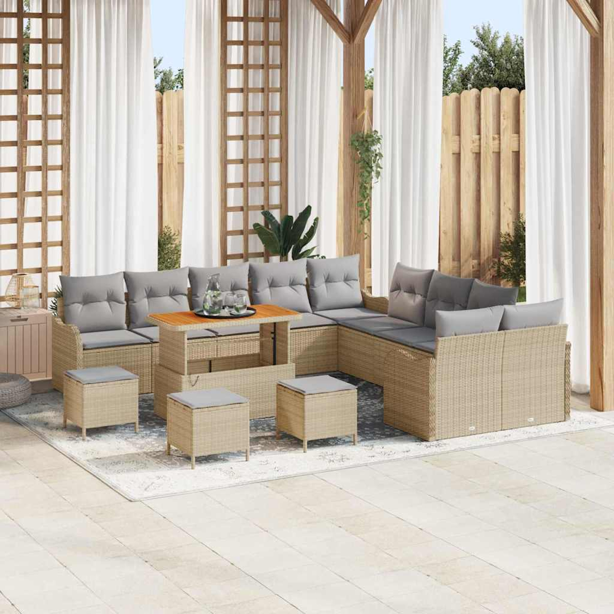 Outdoor-Sitzbereich mit gewebten Möbeln, grauen Kissen, Holztisch und weißen Vorhängen auf einem Teppich.