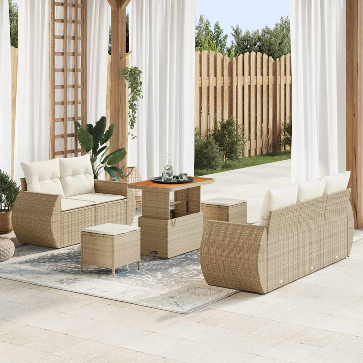 Garten-Terrassenset mit beigen Korbmöbeln, weißen Kissen, einem Couchtisch und einem Teppich, vor Vorhängen und Holzzaun.