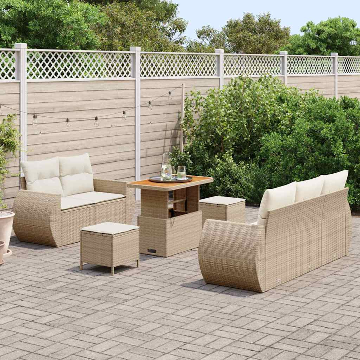 Gartenmöbel-Set aus Korbgeflecht auf einer Terrasse. Enthält Sofa, Stühle, Tisch und Hocker. Hintergrund mit Zaun und Grün.