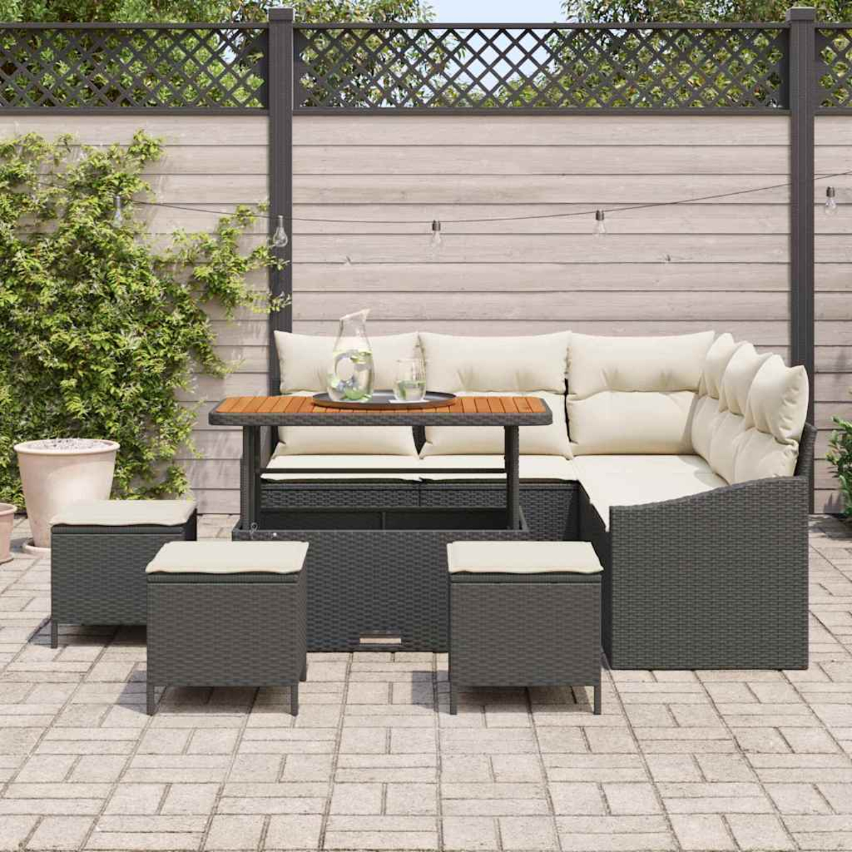 Outdoor-Ecksofa mit Tisch und Hockern auf einer Terrasse. Dahinter ein Holzzaun mit Kletterpflanzen.