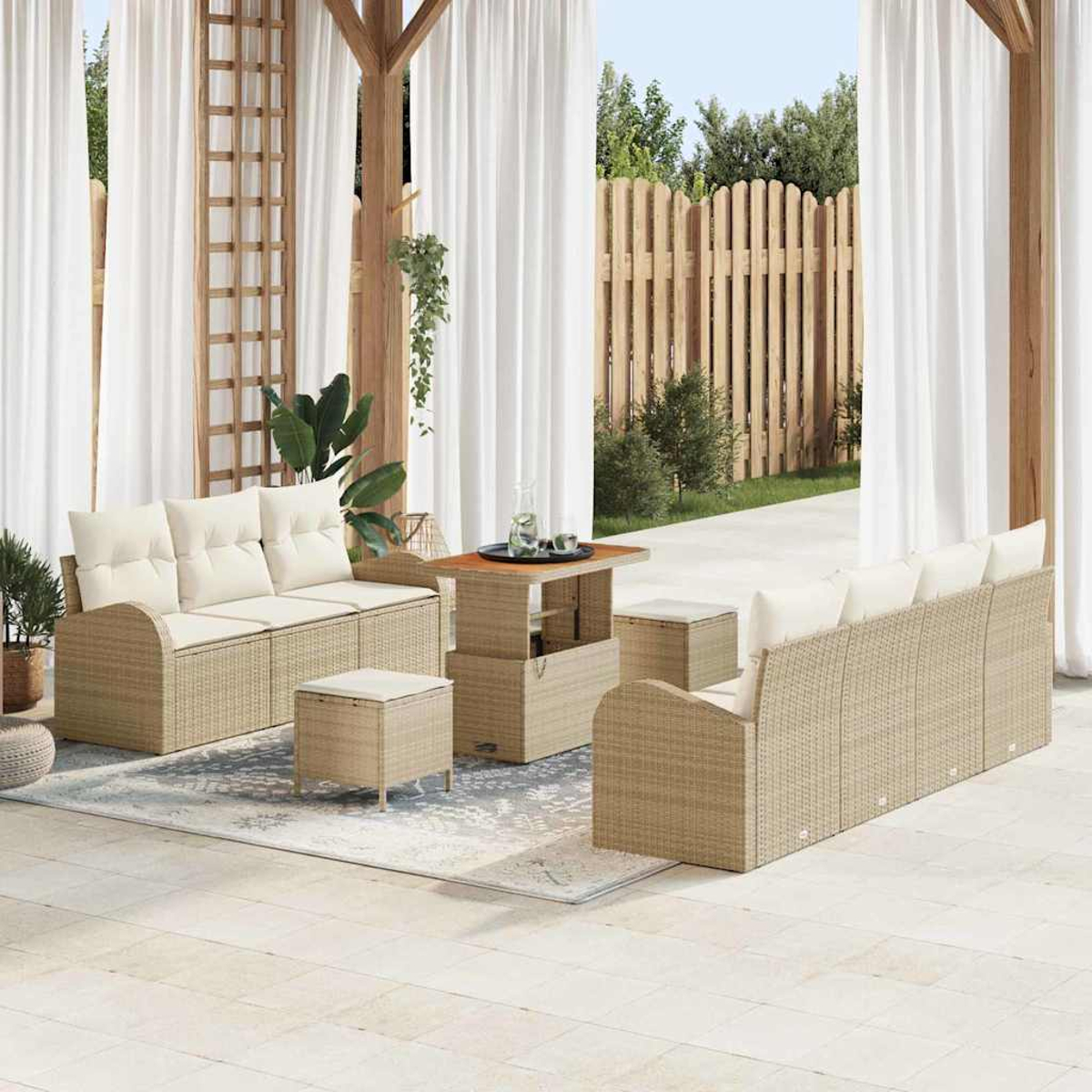 Outdoor-Sitzbereich mit Korbs Sofas, Ottomanen und einem Tisch. Weiße Vorhänge, Holzzaun und Grün im Hintergrund.