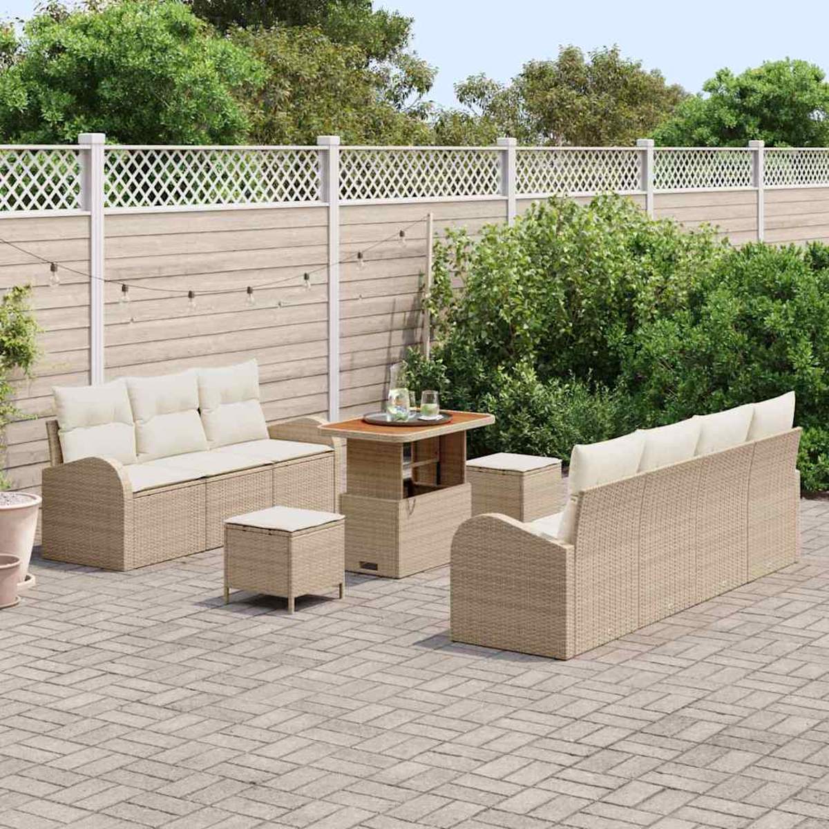 Terrassenmöbel-Set mit beigem Korbmöbeln, cremefarbenen Kissen und einem Holztisch auf einer gepflasterten Terrasse, mit Zaun und Grün im Hintergrund.