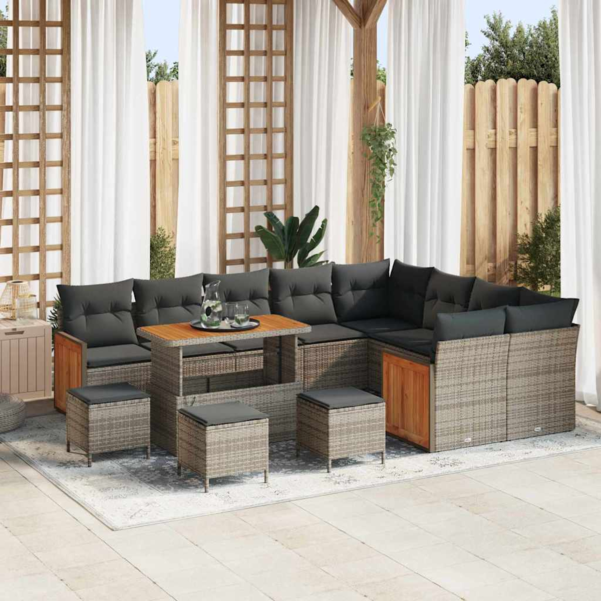 Outdoor-Ecksofa mit grauen Kissen, Holztisch und Hockern. Vorhänge im Hintergrund, und ein Holzzaun, Pflanzen.