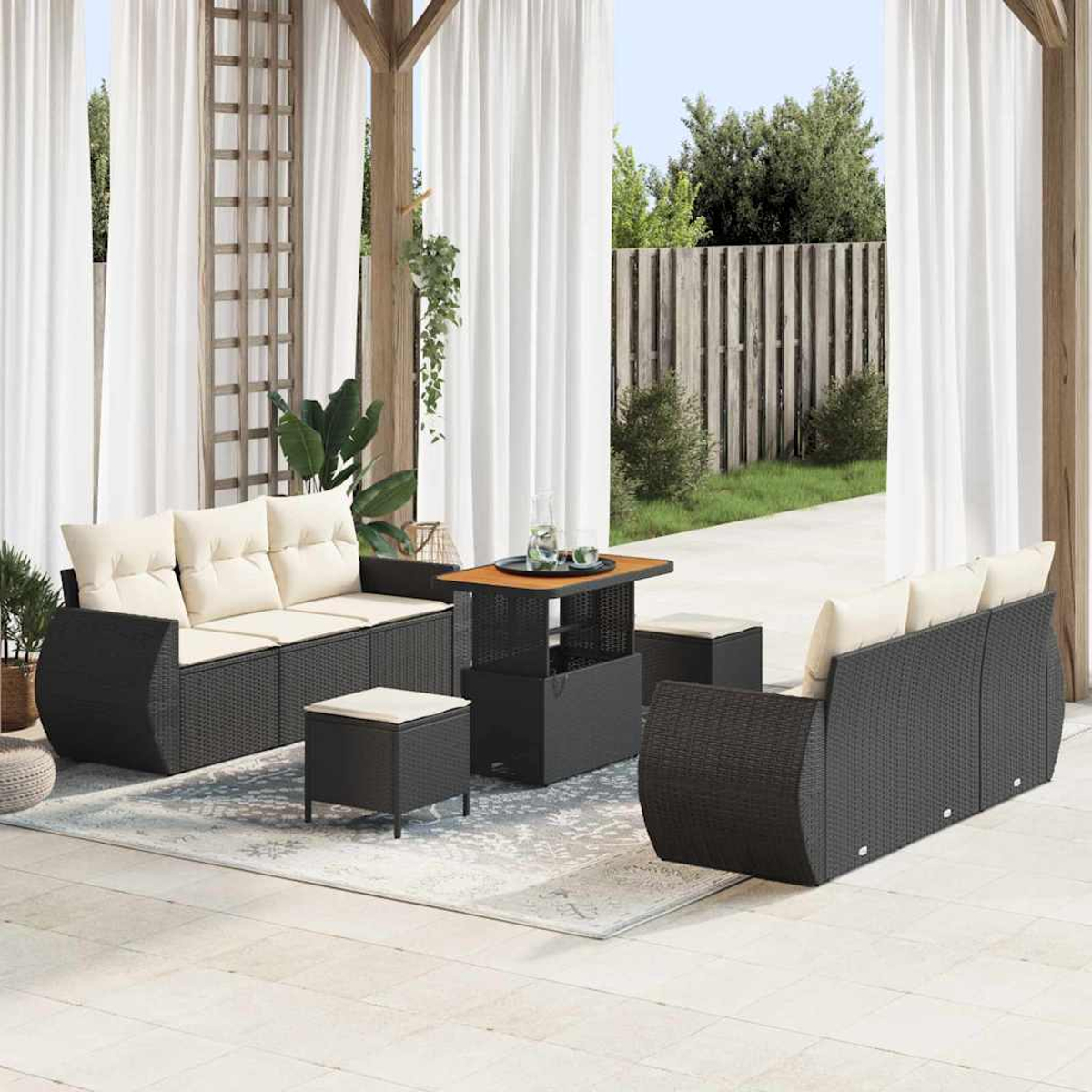 Juego de patio al aire libre con muebles de mimbre negros, cojines beige y una mesa. El fondo muestra una valla, árboles y cortinas blancas.