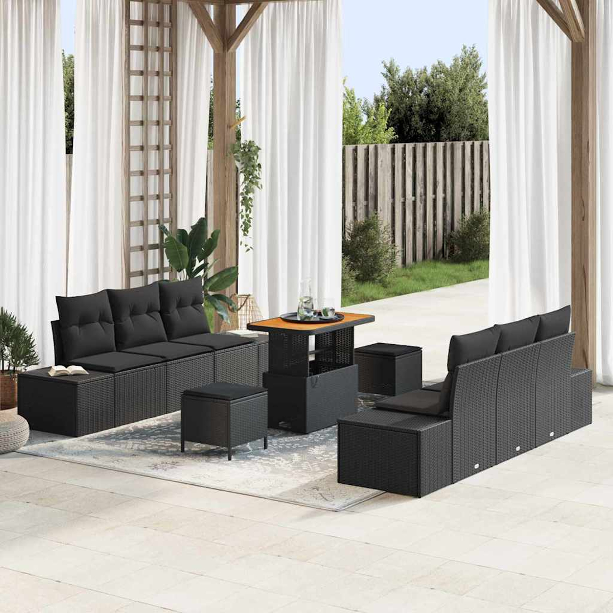 Terrassenmöbel-Set mit schwarzem Korbmöbeln und Kissen. Enthält einen Tisch, Ottomanen und Sofas. Weiße Vorhänge und Grün im Hintergrund.